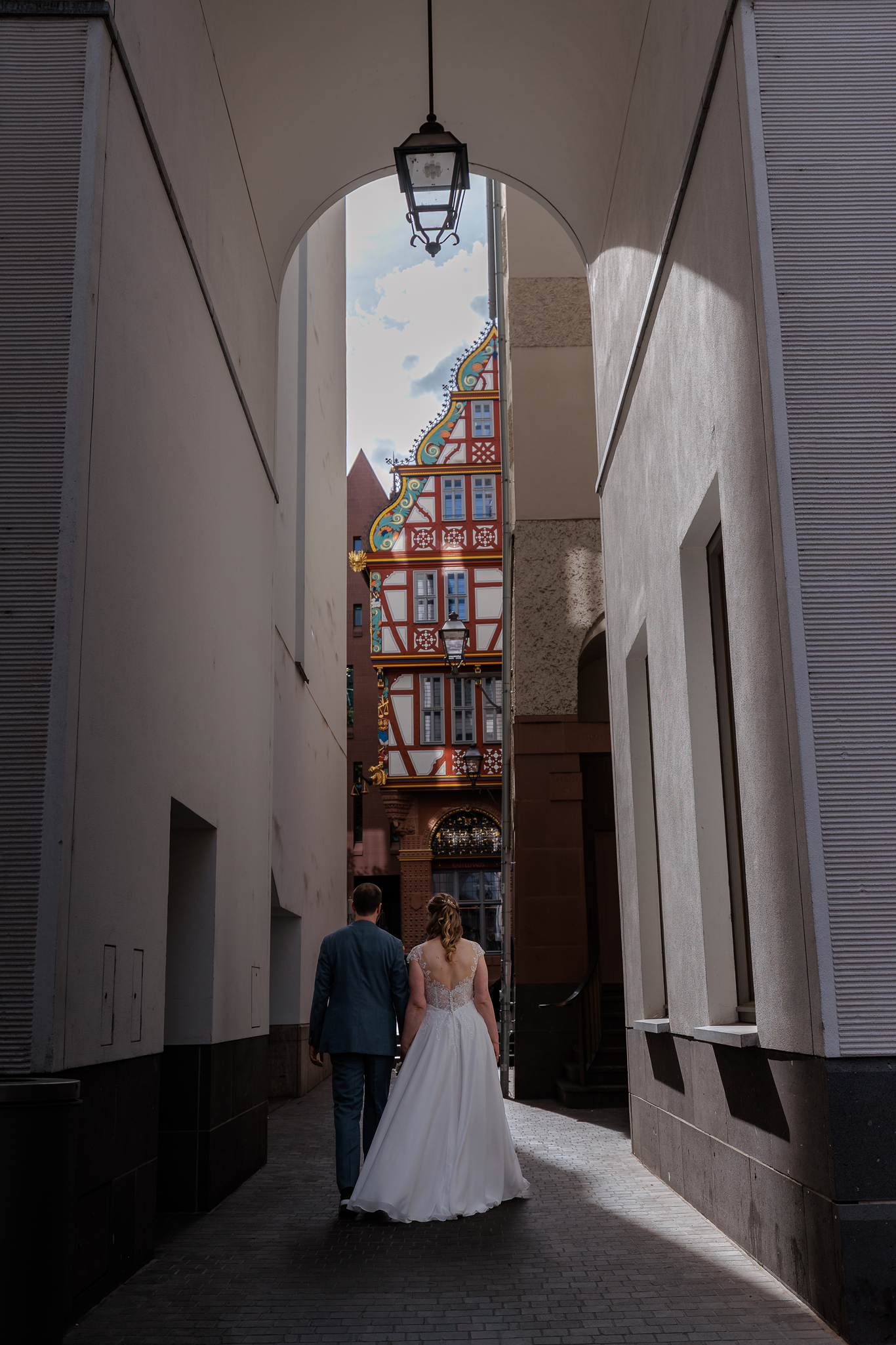 Ein Brautpaar geht durch einen offenen Bogen in der neuen Alstadt Frankfurt, im Hintergrund ein historisches Fachwerkhaus.