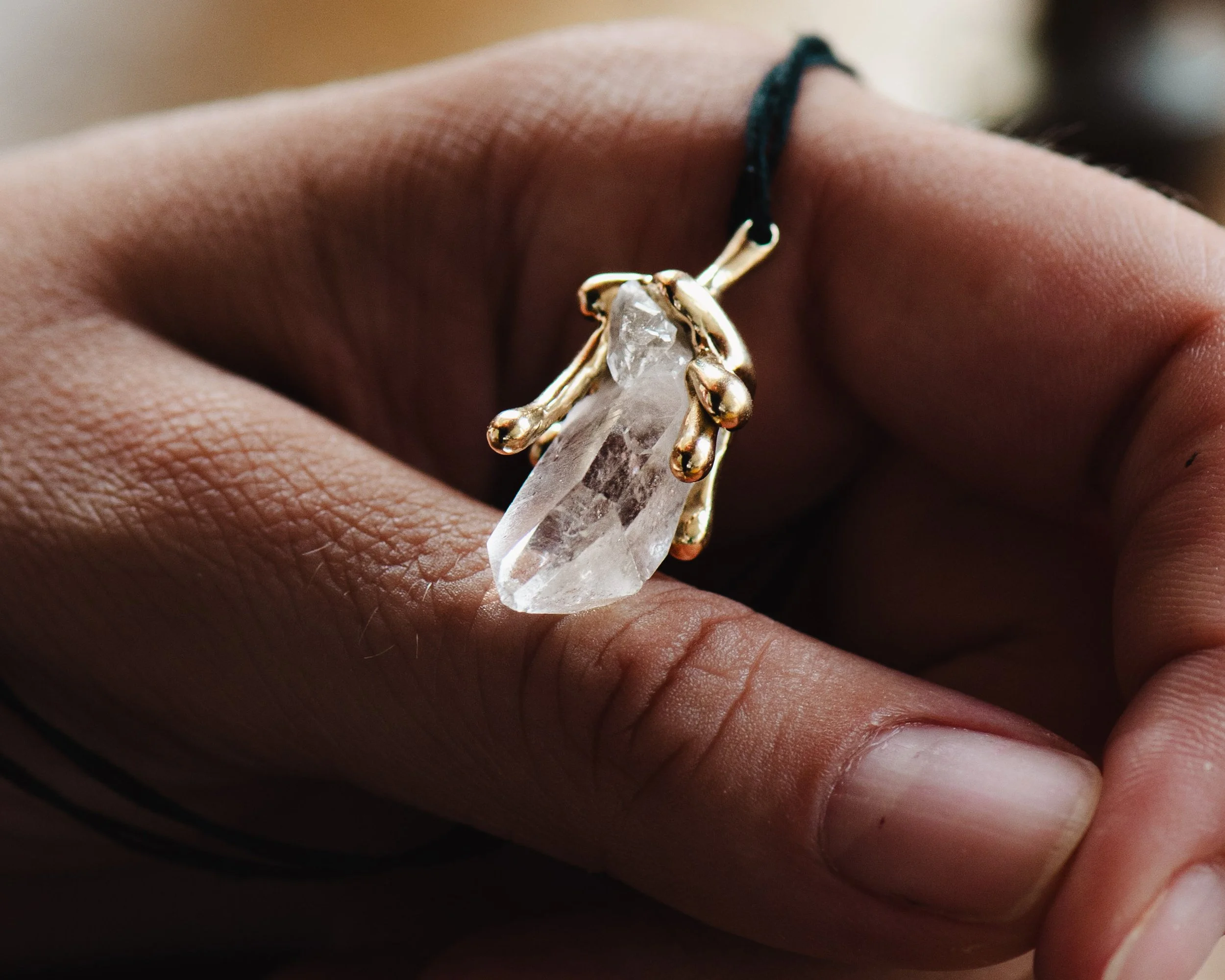 Hand hält einen goldenen Schmuckring mit einem großen, transparenten Kristallanhänger.