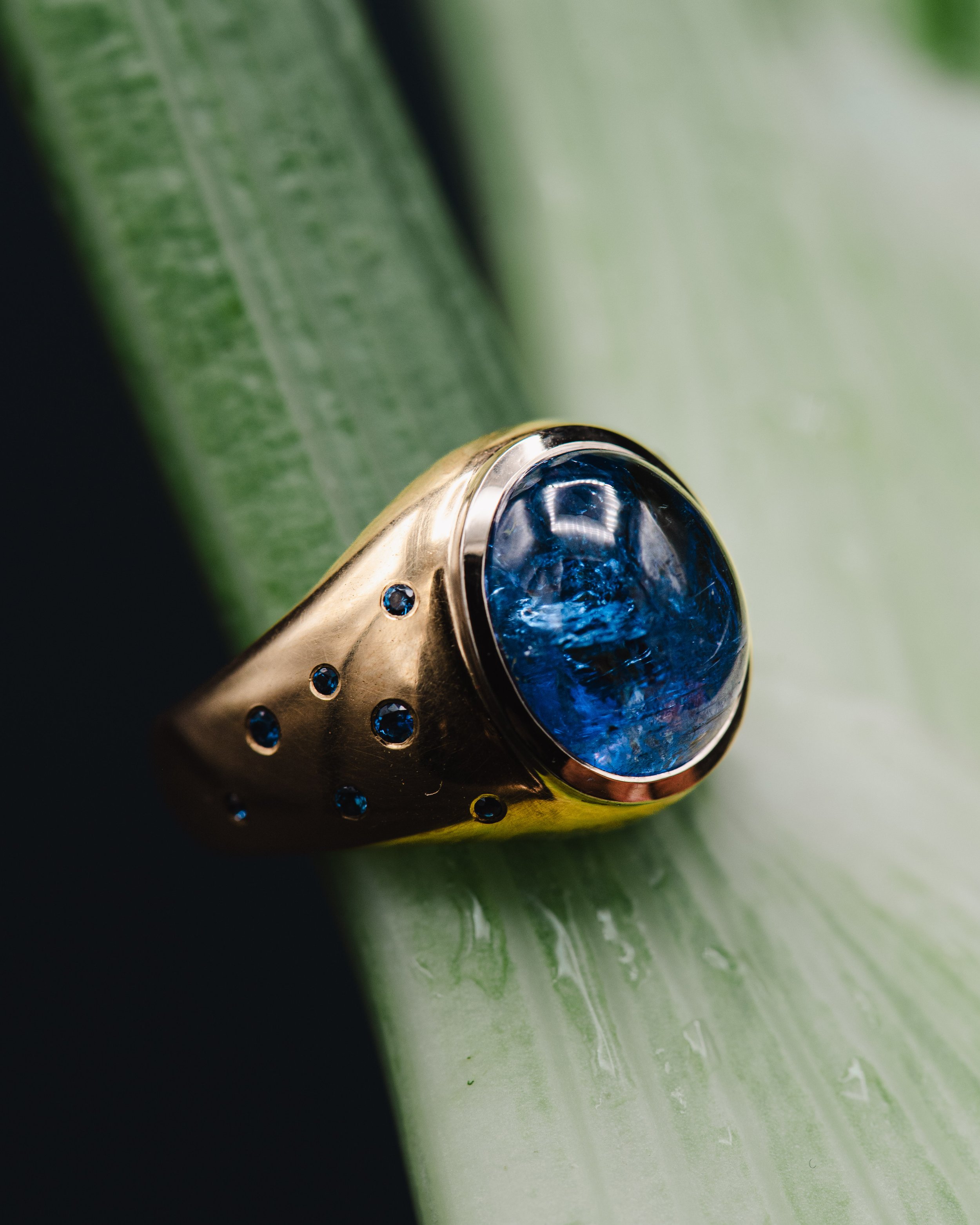 Ein goldener Ring mit blauer Kuppel auf einer grünen Oberfläche.