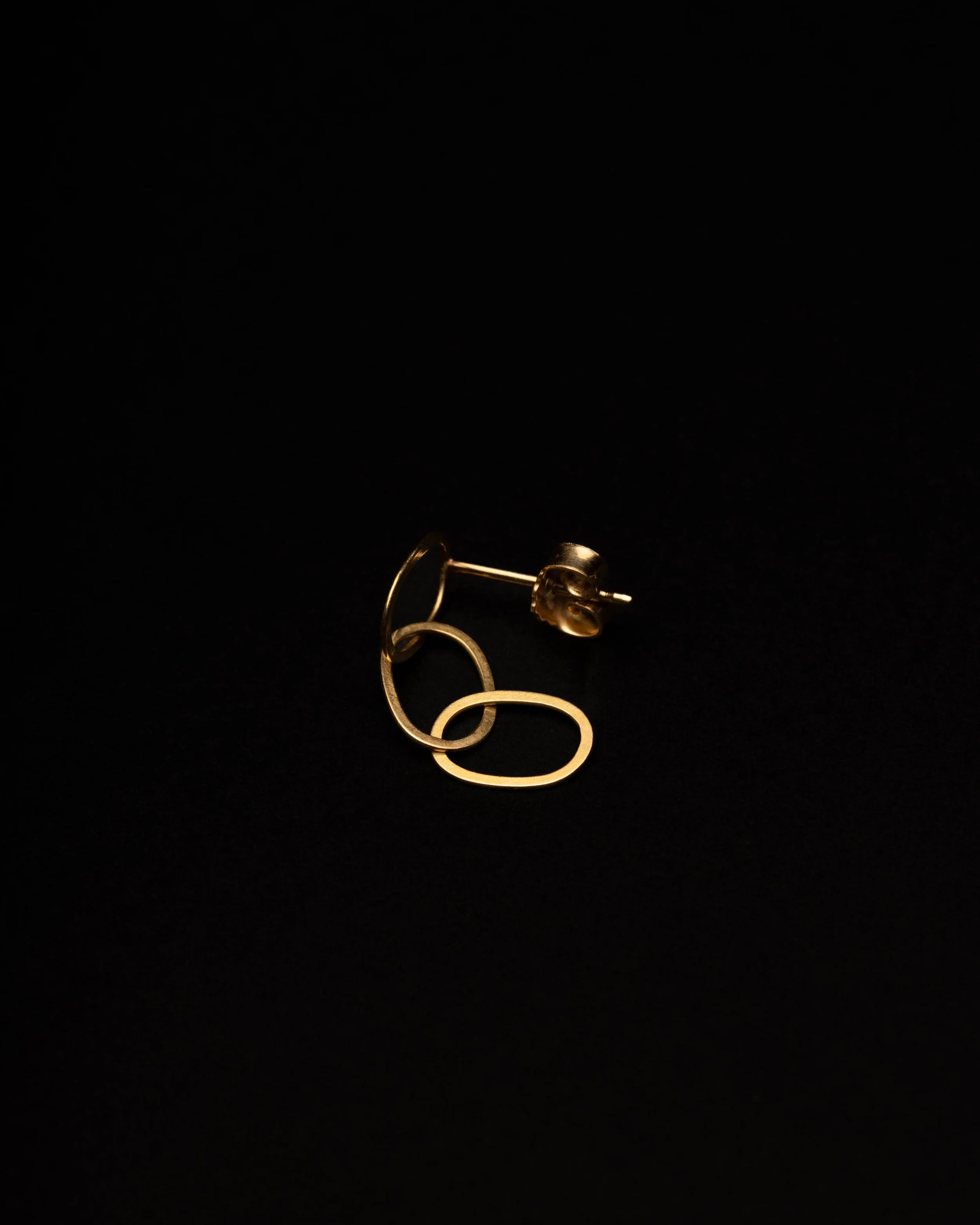 Goldene Ohrstecker mit zwei interconnecteden ovalen Formen auf schwarzem Hintergrund.