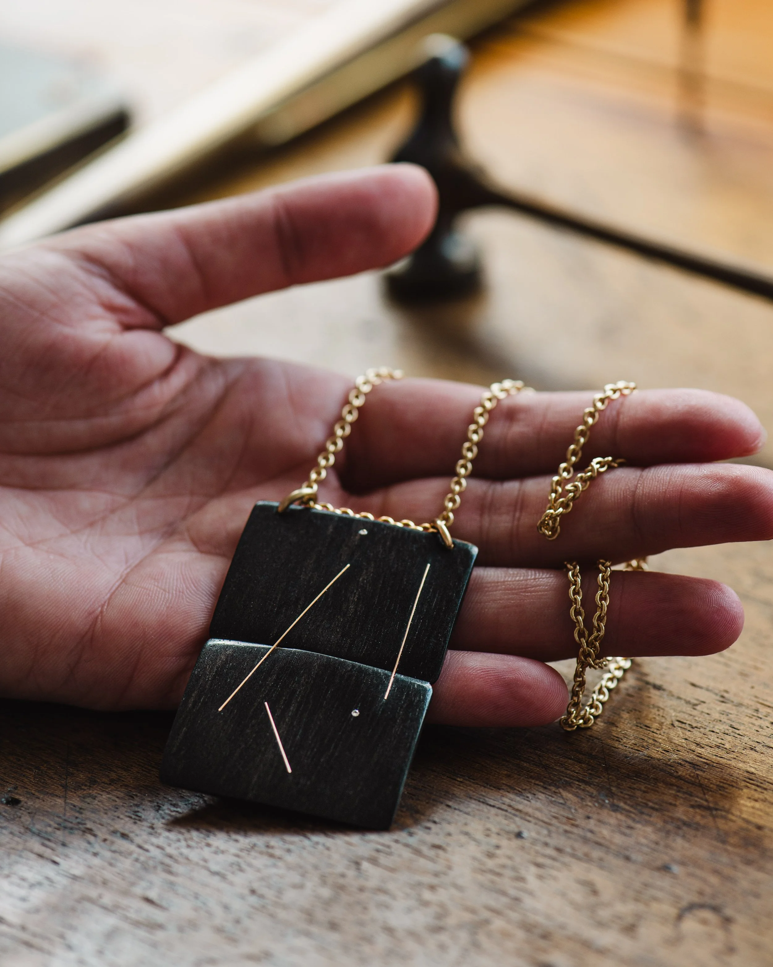 Hand hält eine schwarze Kette mit Anhänger auf einem Holztablett.