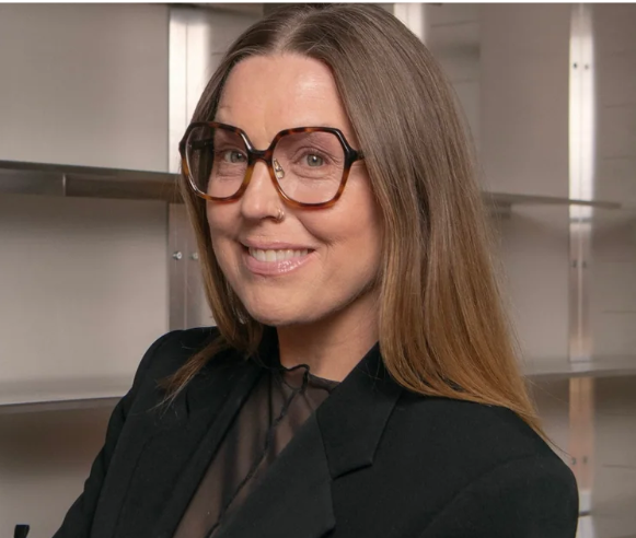 nina färdig i närbild står framför vägghängda hyllor i sin butik.