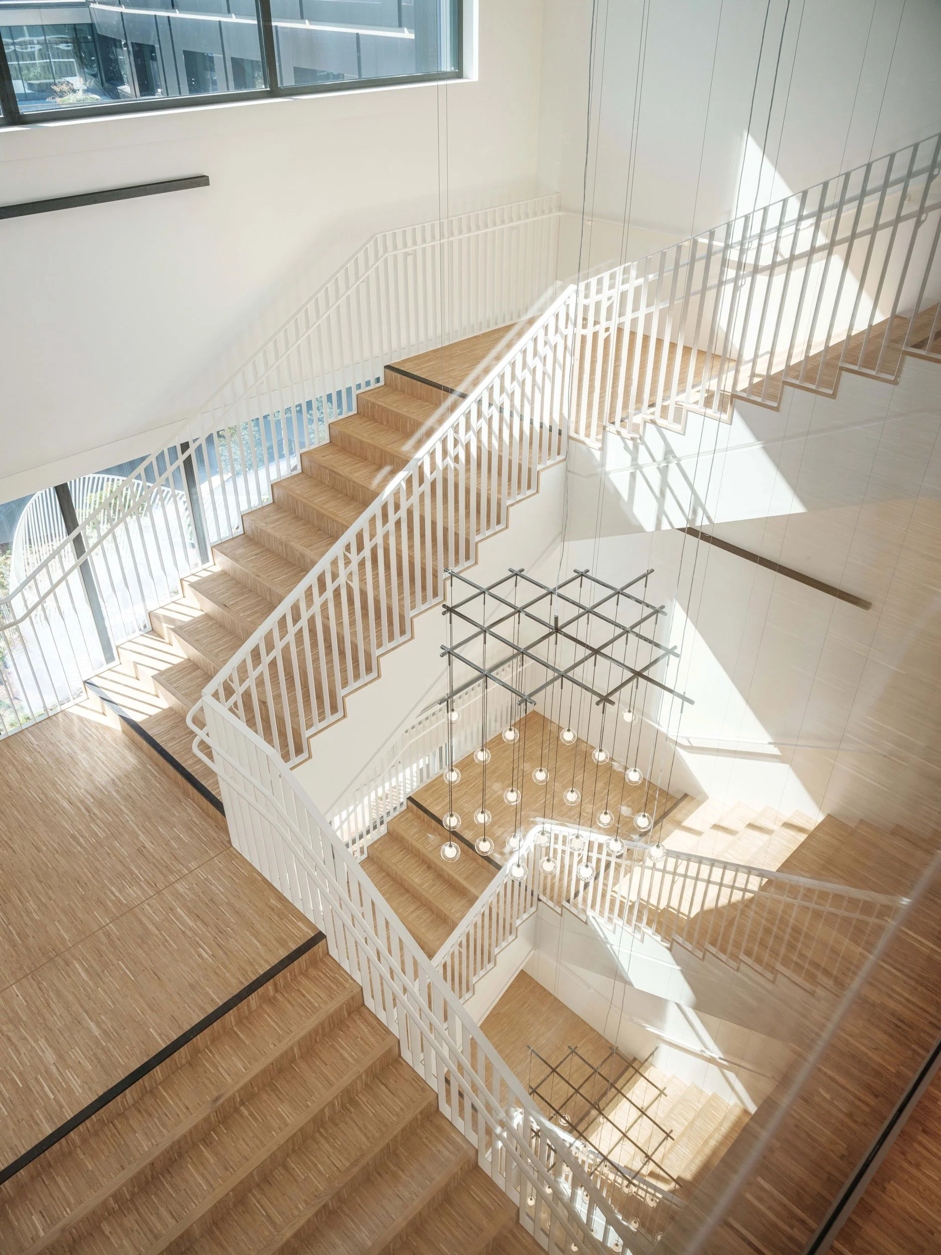 Modern interior staircase with wooden steps, white railings, and a geometric chandelier in a well-lit space.