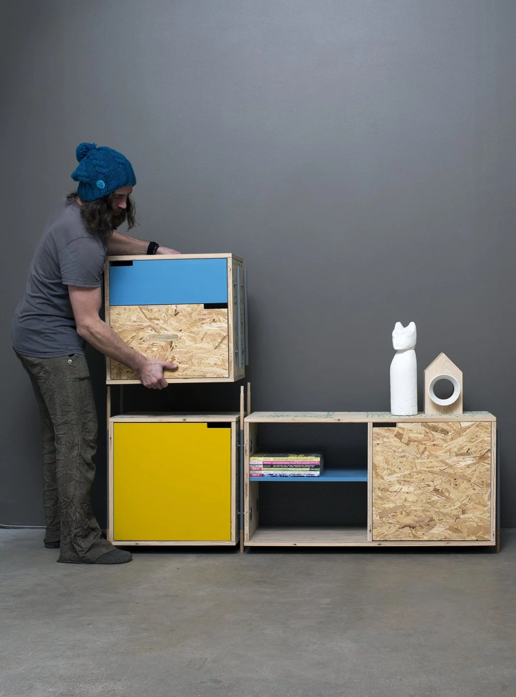 Person organizing modular storage unit with blue and yellow doors, featuring a decorative vase and wooden ornaments on top.
