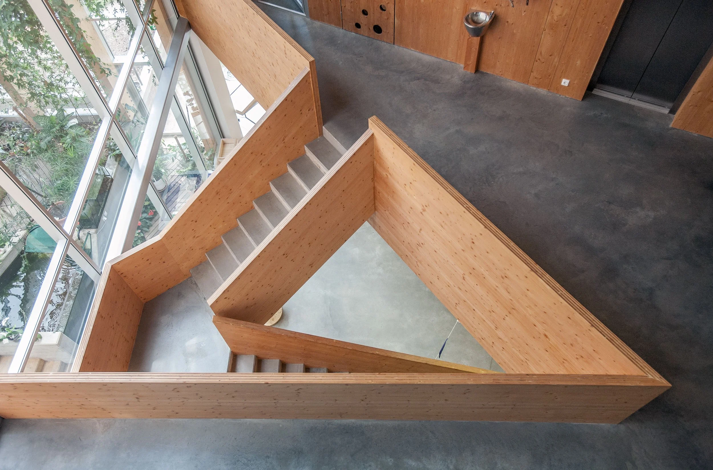 Top view of a modern staircase with wooden walls and glass windows, surrounded by greenery.