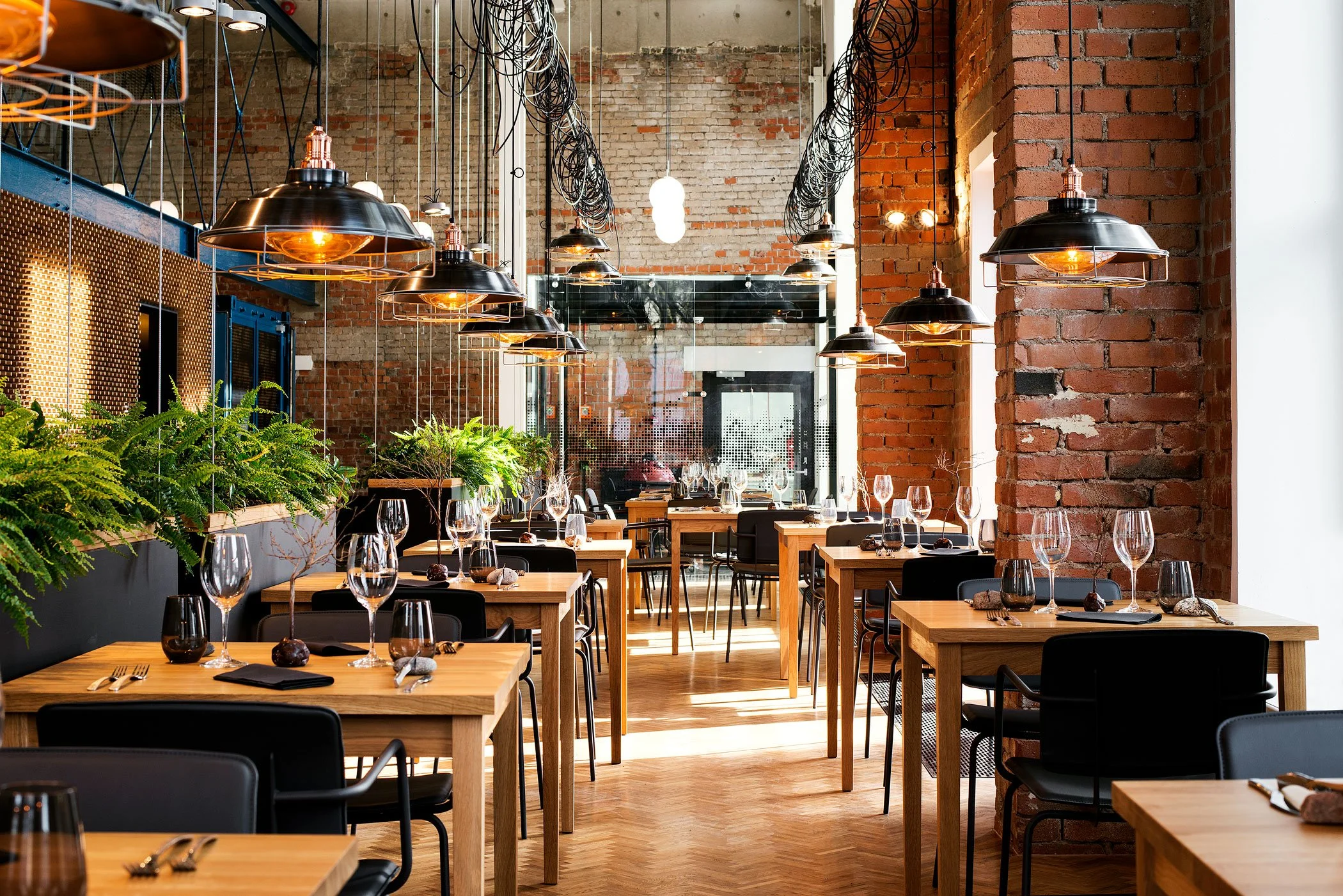 Modern industrial-style restaurant interior with brick walls, wooden tables, and hanging lights.