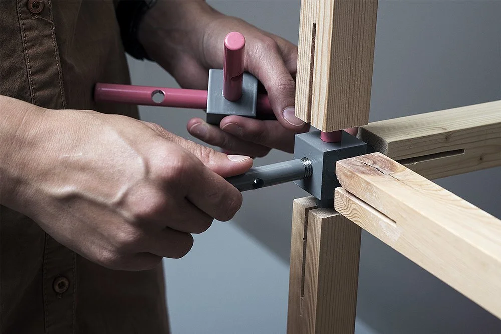 A person assembling wooden beams using metal connectors and tools.