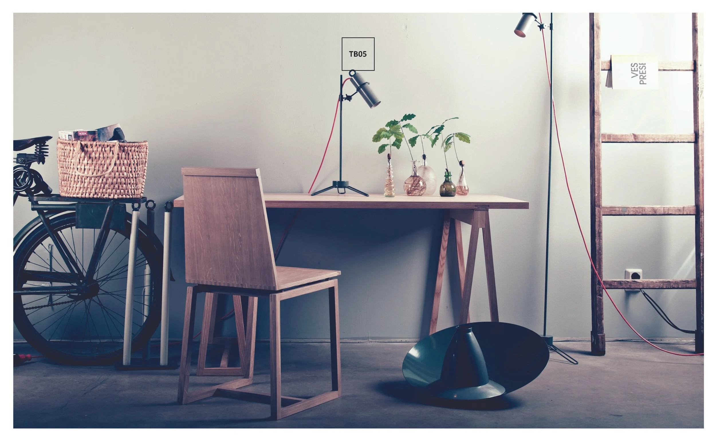 Modern minimalist workspace with wooden desk, wooden chair, table lamp, potted plants, bicycle with basket, wooden ladder, and a large floor cone light fixture.