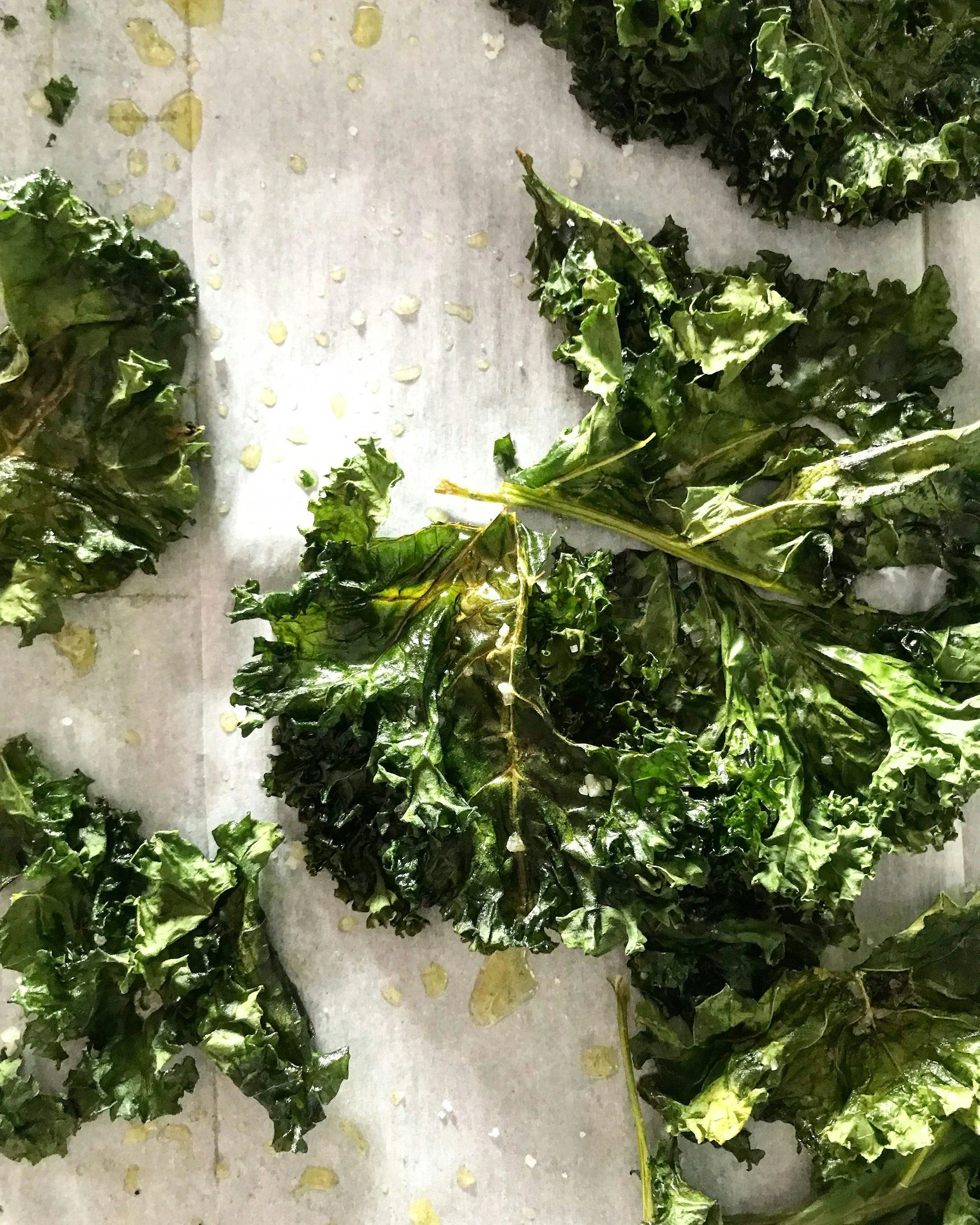 Freshly washed kale leaves on a white surface with some water droplets and torn pieces.