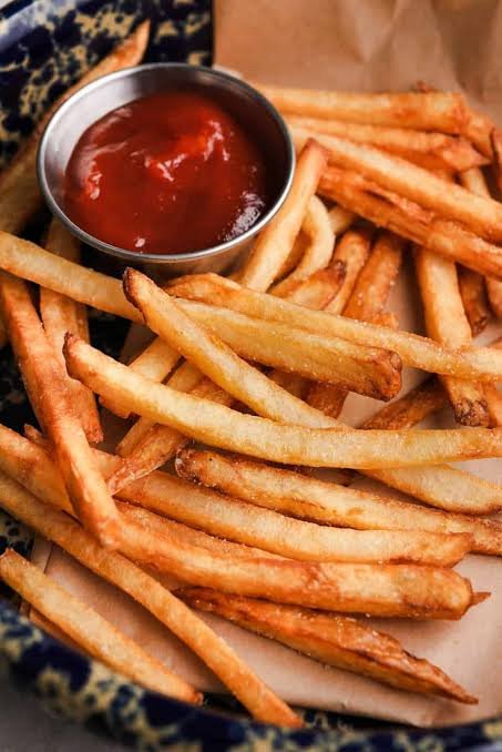 A basket of French fries with a small cup of ketchup.
