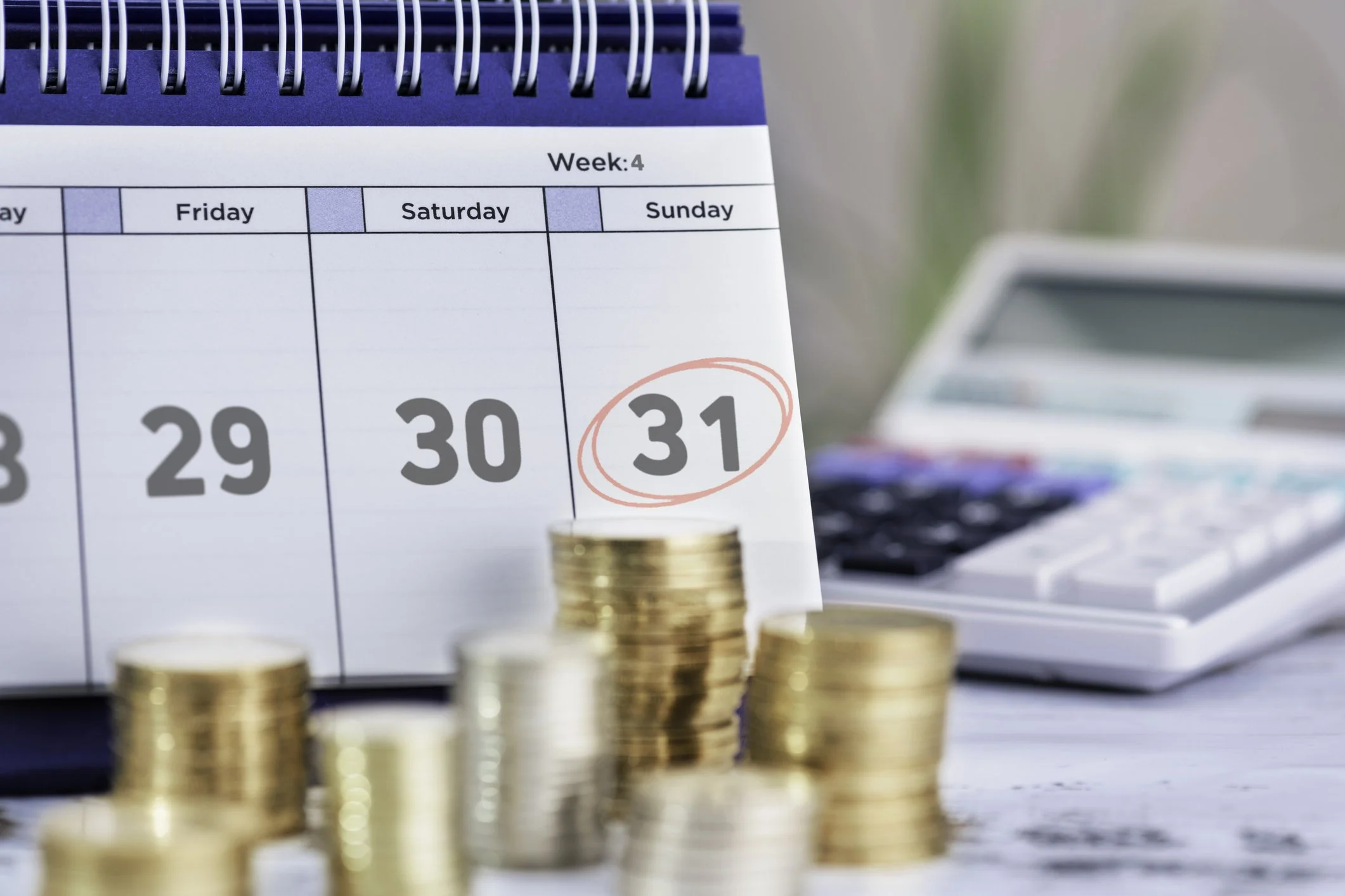 Ein Kalender zeigt den 31. Tag eines Monats. Daneben liegen auf einem Tisch Münzen und ein Taschenrechner.
