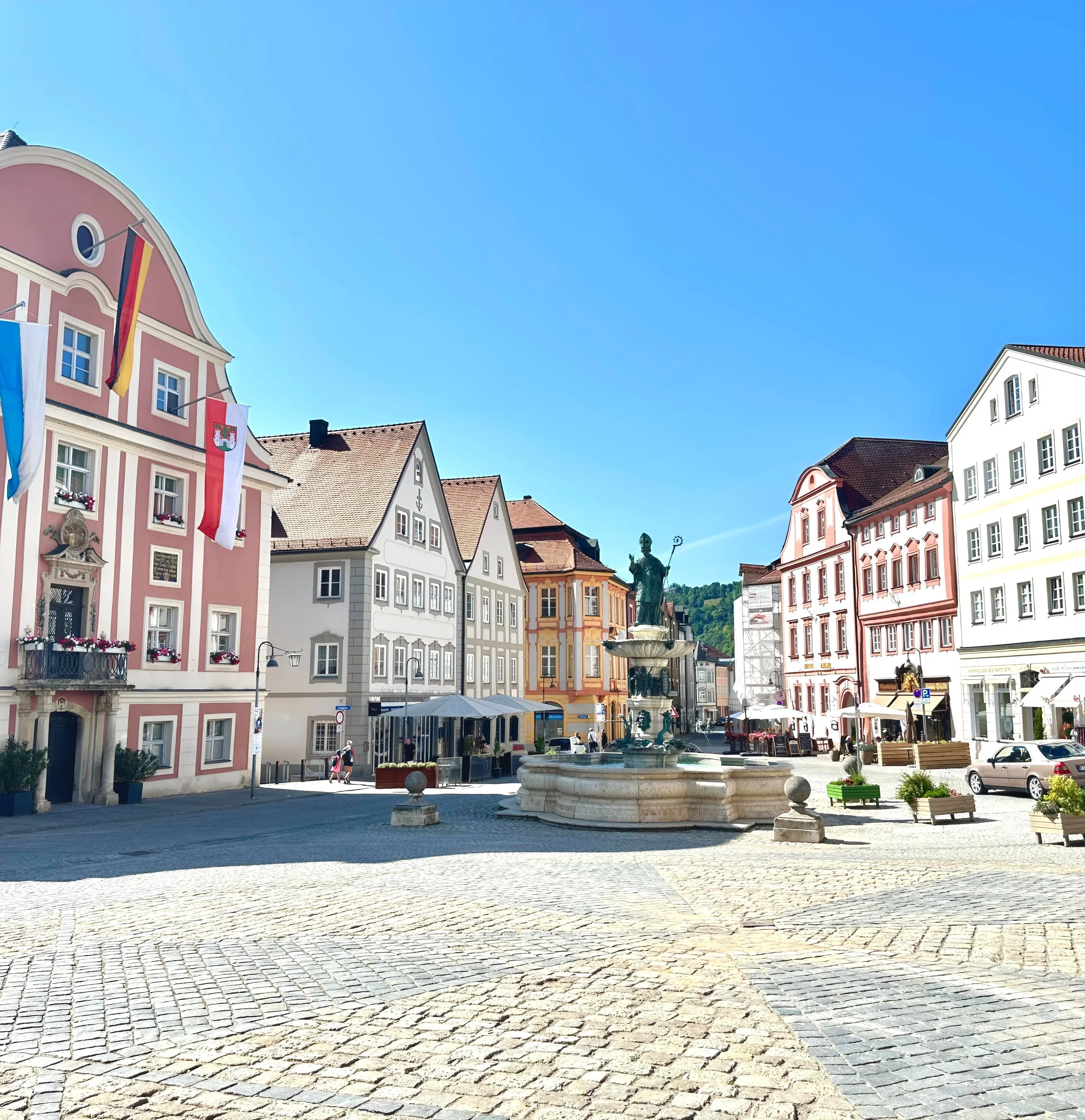Blick auf einen mittelalterlichen Marktplatz mit bunten Gebäuden, Brunnen und einem Freiheitsdenkmal, bei schönem Wetter