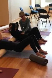 People practicing rolling using SpineTune method with foam rollers in a studio with chairs in the background.