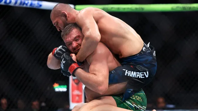 Two mixed martial artists fighting inside the octagon, with one executing a grapple on the other.