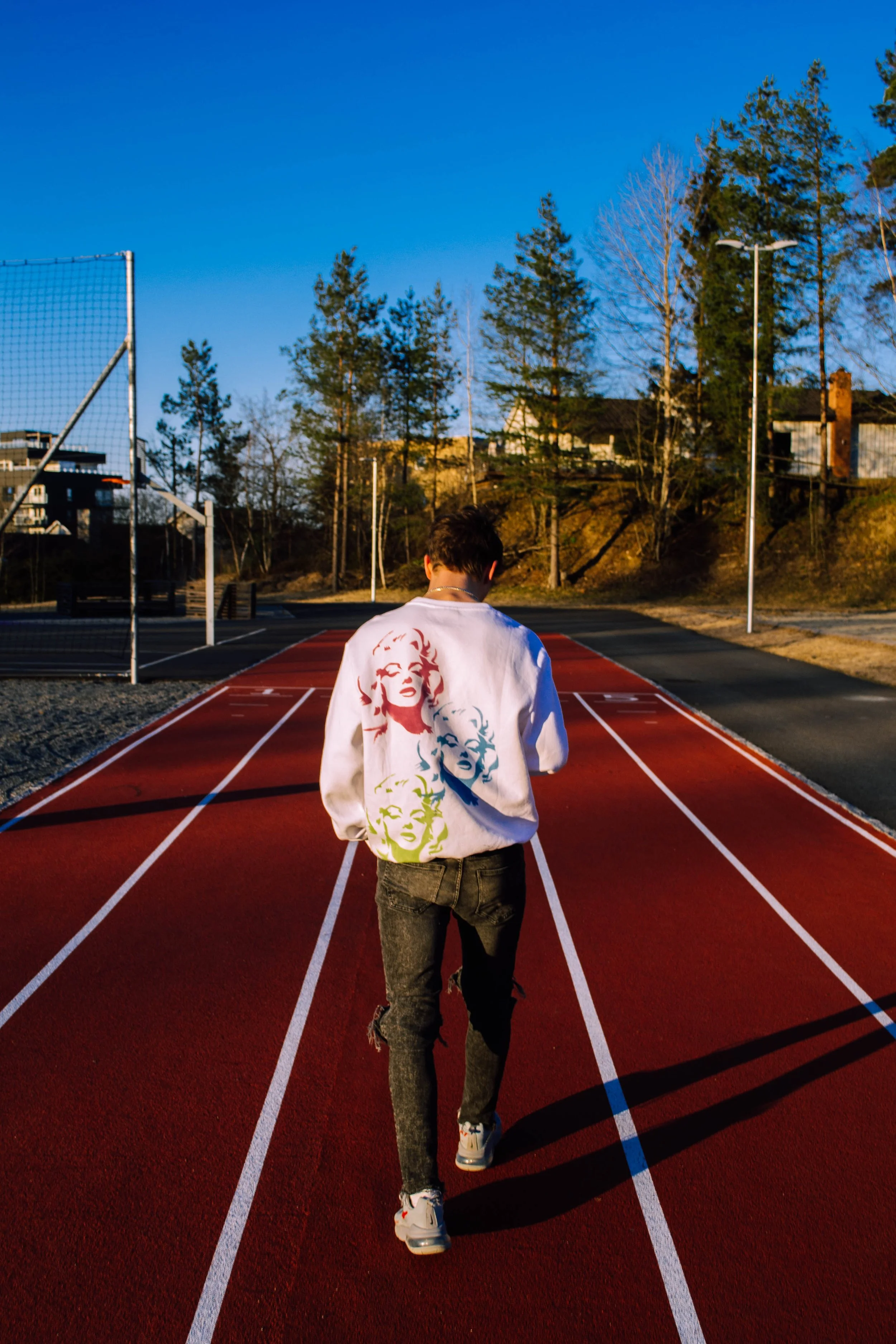 En person går på en utendørs løpebane med blå himmel og trær i bakgrunnen.