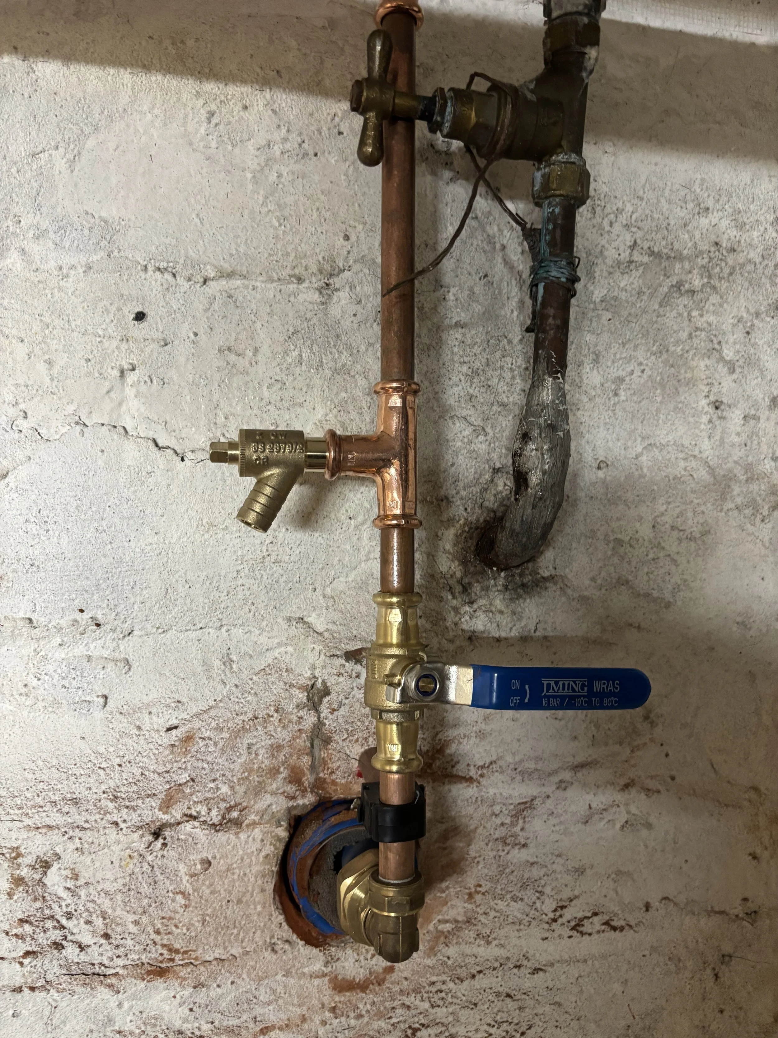 Close-up of plumbing pipes and a water shut-off valve on a concrete wall.