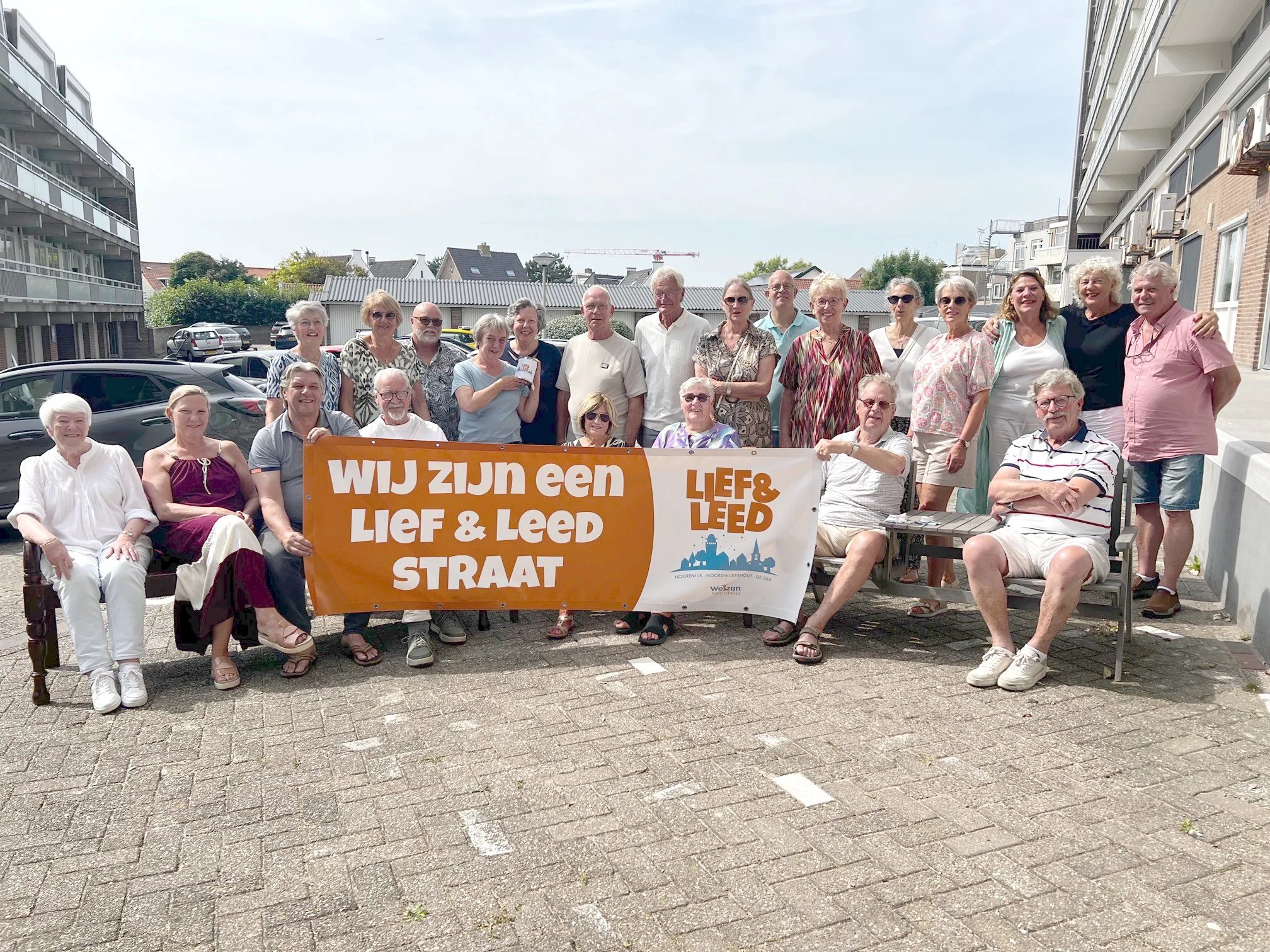 Een groep ouderen poseert buiten op een straat, met een banner die zegt 'WIJ ZIJN EEN LIEF & LEED STRAAT'.