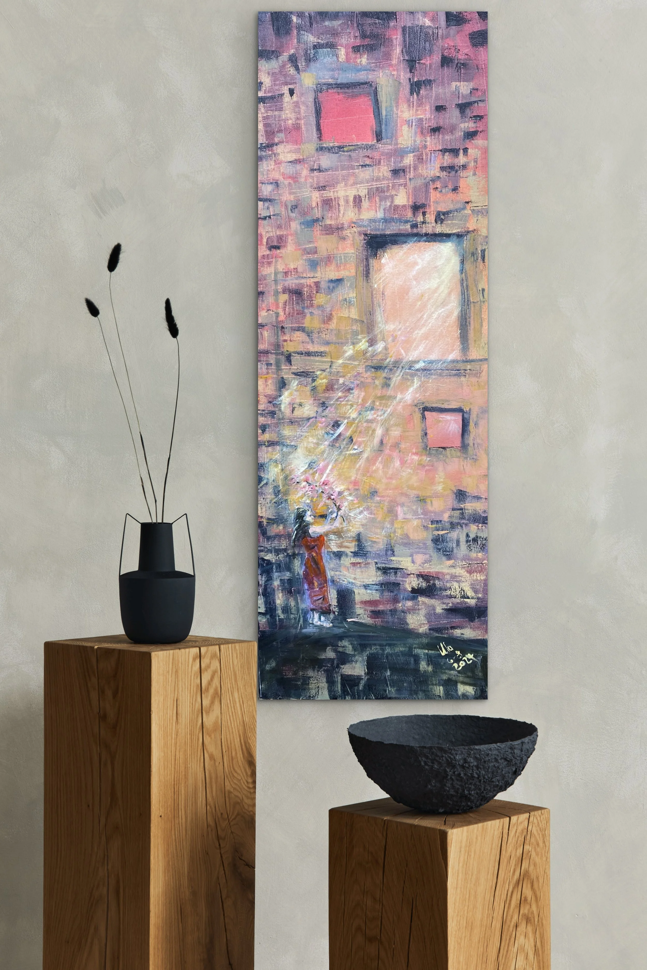 Kunstwerk in einem modernen Raum, zeigt eine abstrakte Stadtansicht mit Fenstern und einem Mädchen, das Wasser sprüht. Zwei Holzpodeste mit schwarzen Dekorationsgegenständen, eine Vase mit Trockenblumen, und die Wand im Hintergrund ist hell.