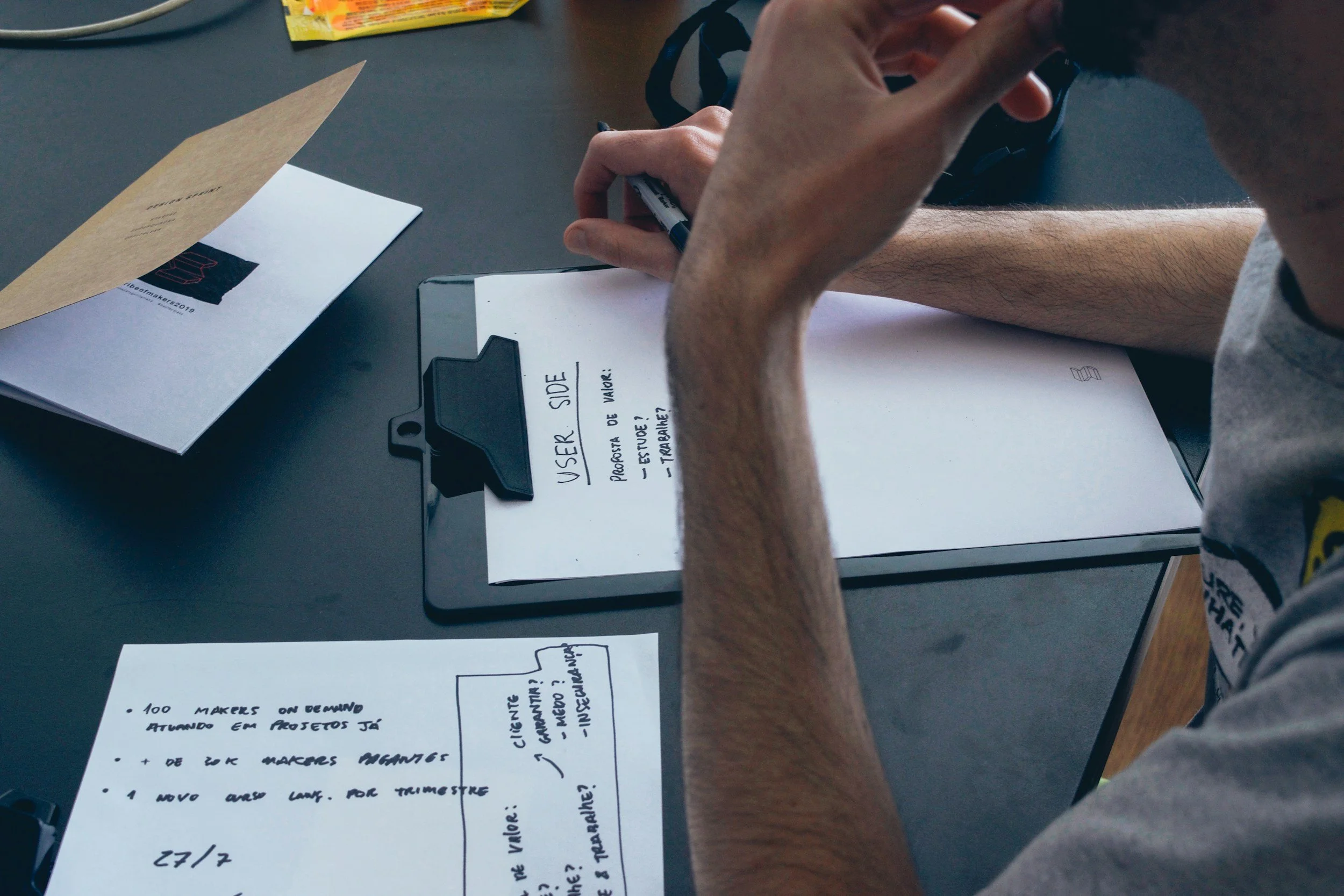 A person sitting at a desk reviewing notes, with papers, a clipboard, and an envelope on the desk. Tutoring.