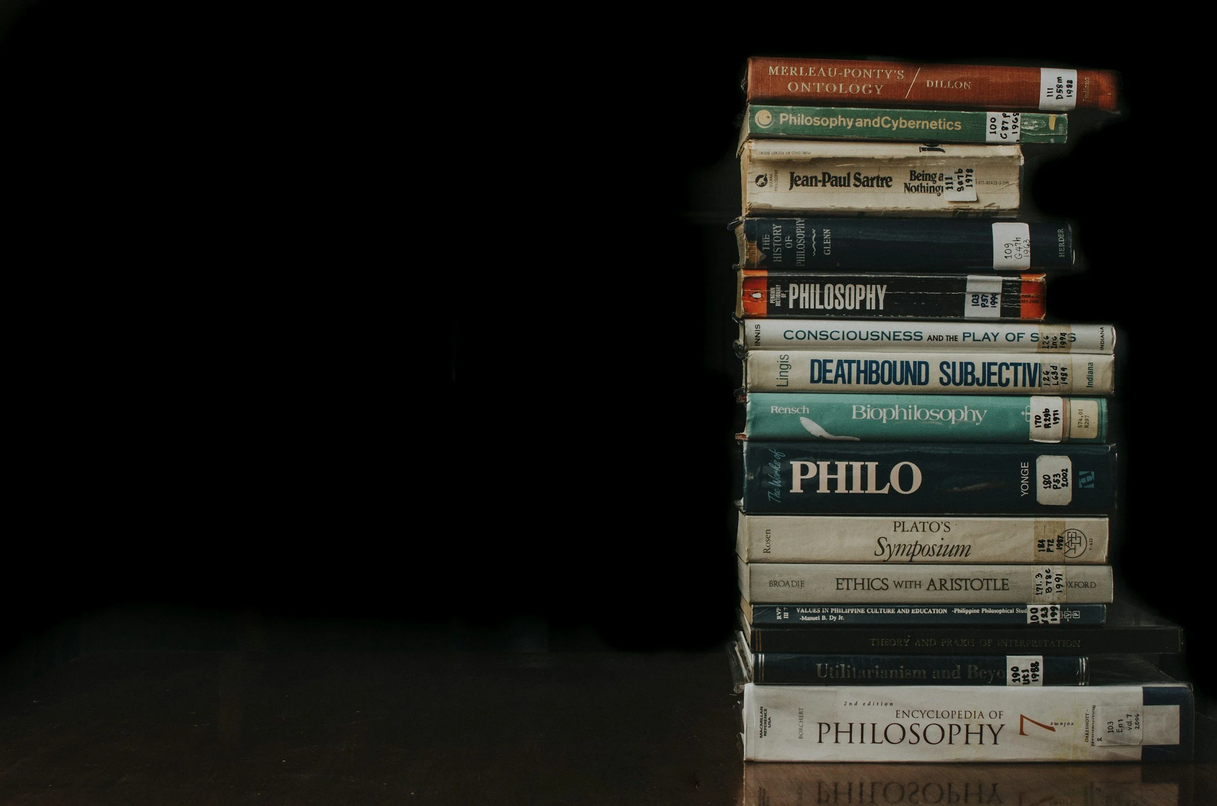 Stack of philosophy and ethics books on a dark surface against a black background. RS tutor. Philisophy tutor.