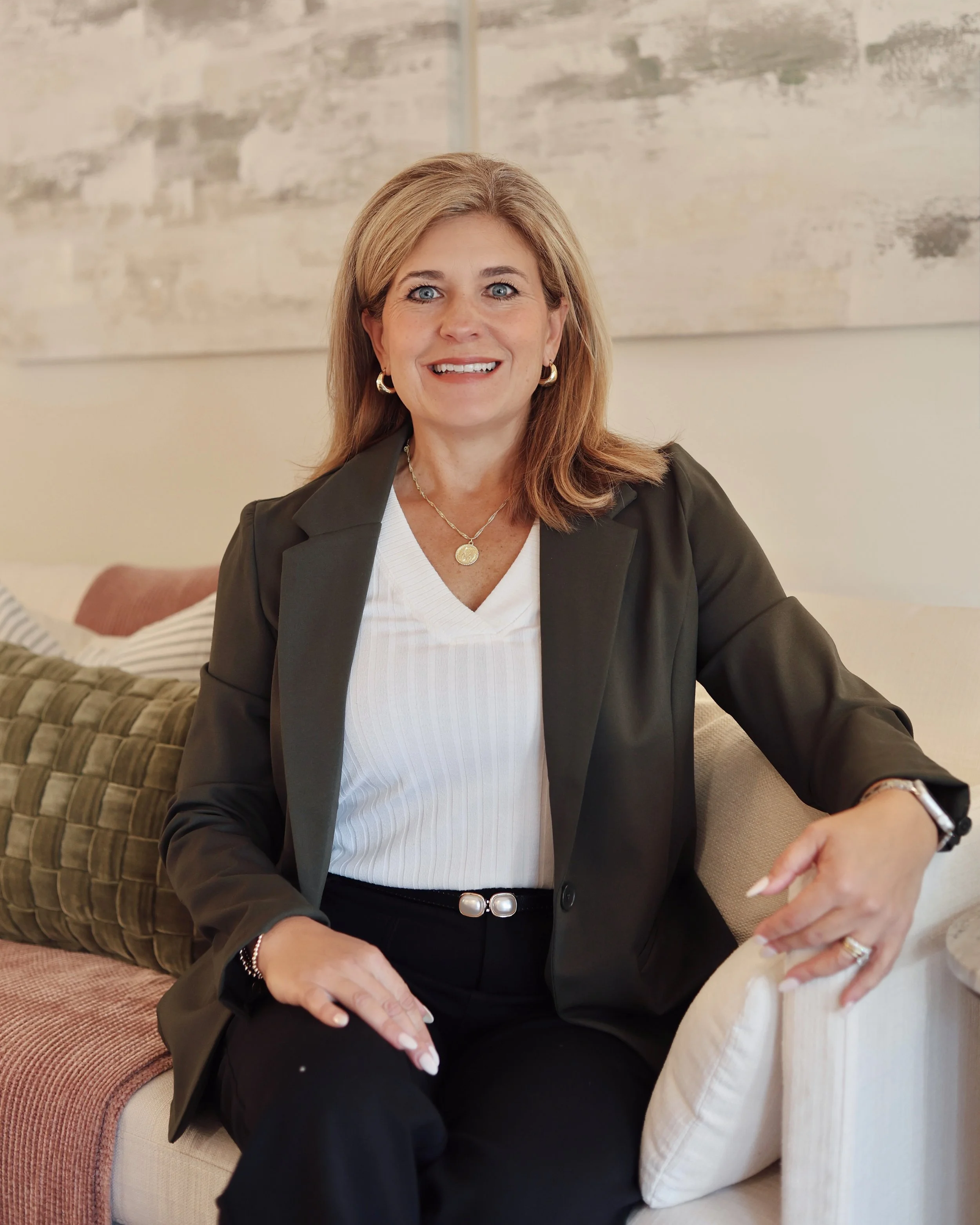 A woman in a suit smiling, standing with arms crossed.
