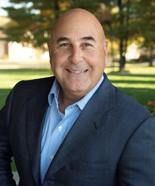 Black and white portrait of a woman with short hair wearing a sleeveless top and necklace, smiling at the camera.