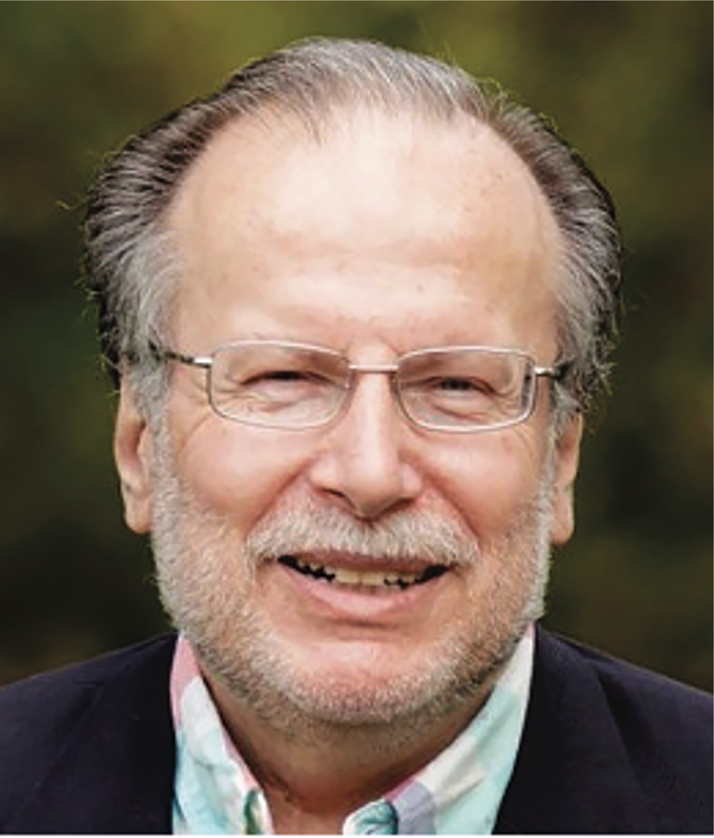 A smiling elderly man with glasses, gray hair, and a beard, wearing a dark jacket over a pastel-colored shirt, outdoors with a blurred natural background.