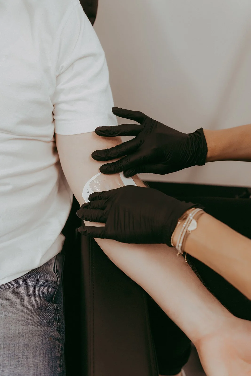 Person receiving a vaccination shot in their upper arm from healthcare worker wearing black gloves.
