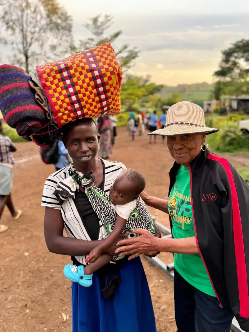 Mission volunteer posing with a local holding a baby while traveling through rural Kenya