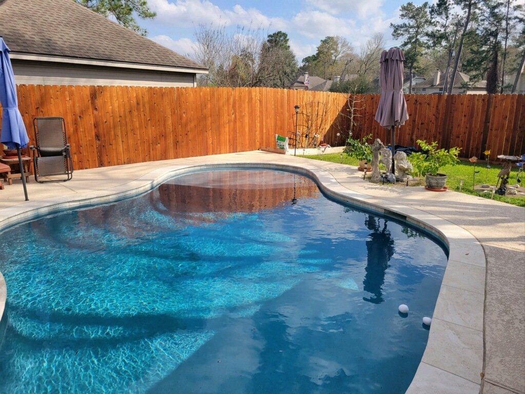 Backyard with swimming pool, patio chairs, wooden fence, and garden with plants.