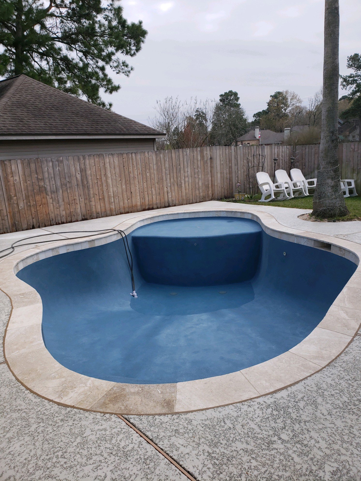 Empty swimming pool in backyard with patio chairs and wooden fence