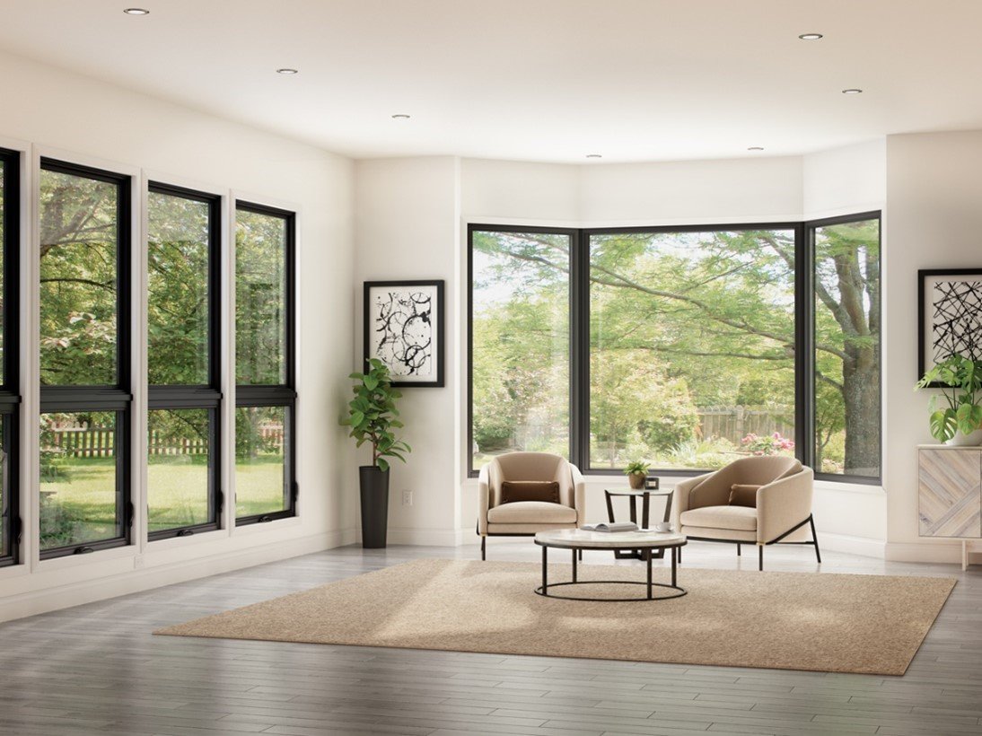 Modern living room with large windows, beige chairs, round coffee table, potted plants, and abstract wall art.