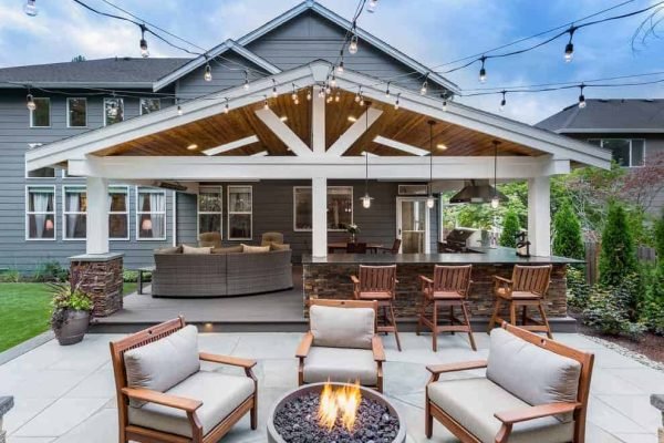 Outdoor patio with a covered seating area, fire pit, and wooden furniture in a backyard setting.