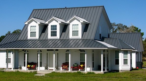White two-story house with a metal roof, three dormer windows, and a front porch with chairs.
