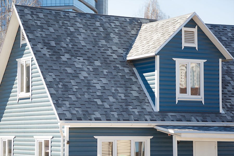 Close-up of a blue house with a gray shingle roof, showcasing windows and architectural design details.
