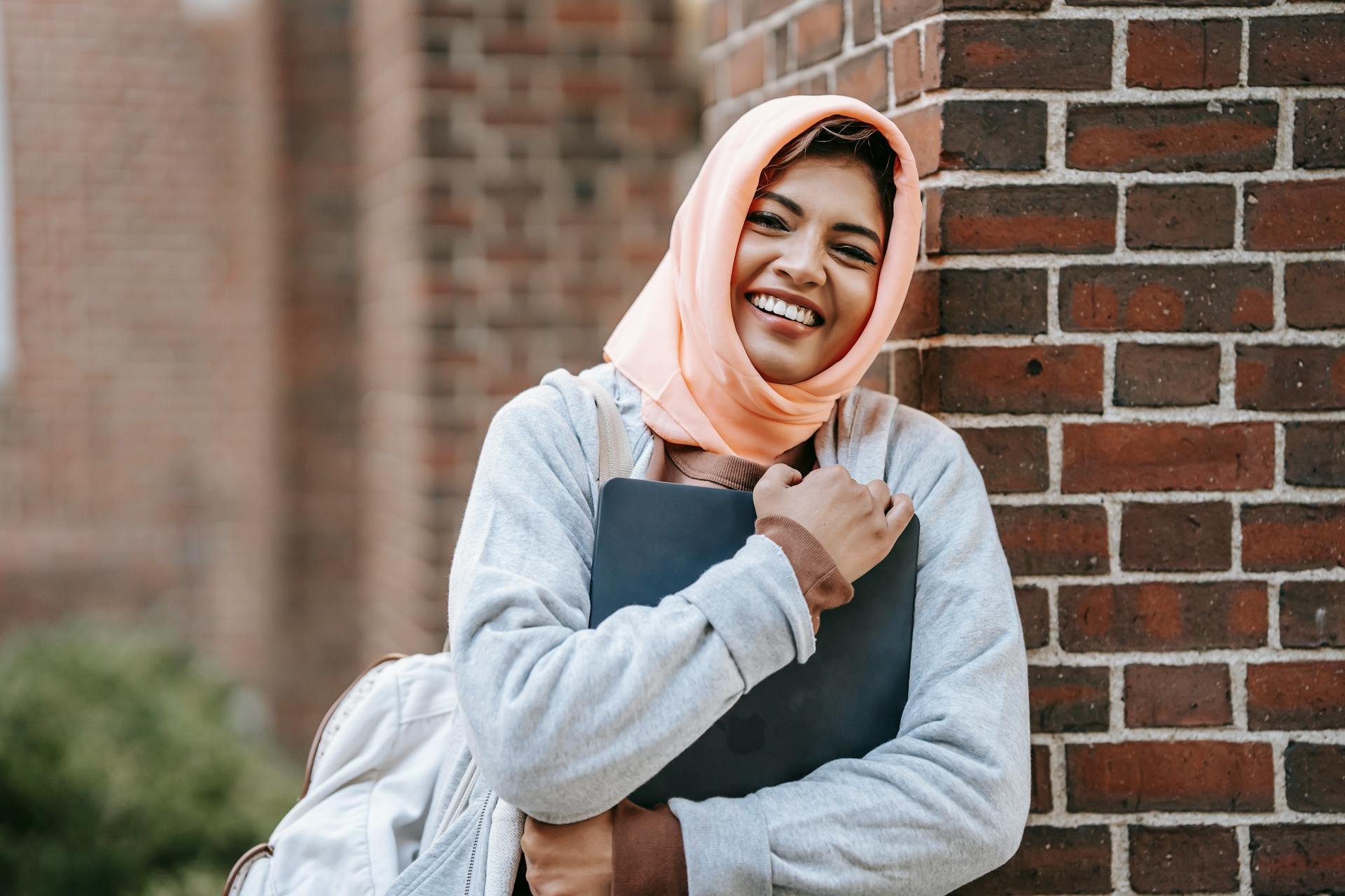 an international student wears a head covering and smiles at the camera, holding her school books. She is covered by health insurance for international students.
