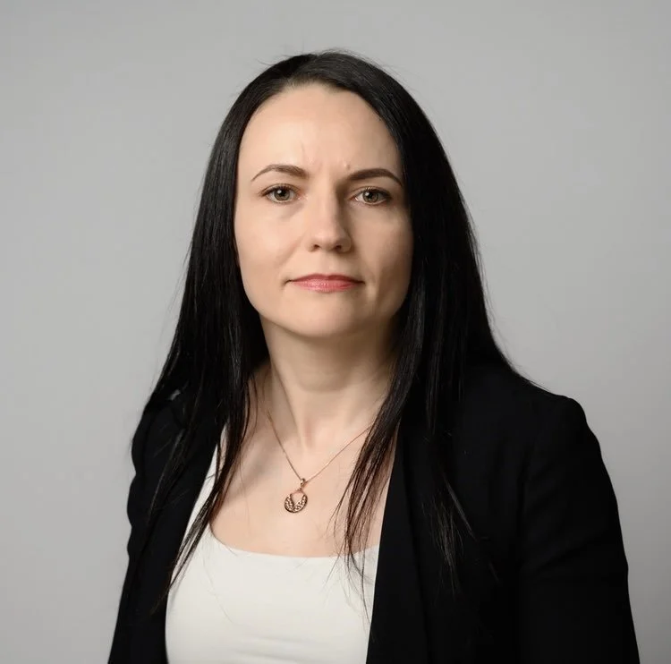 Woman with long black hair wearing a black blazer and white top