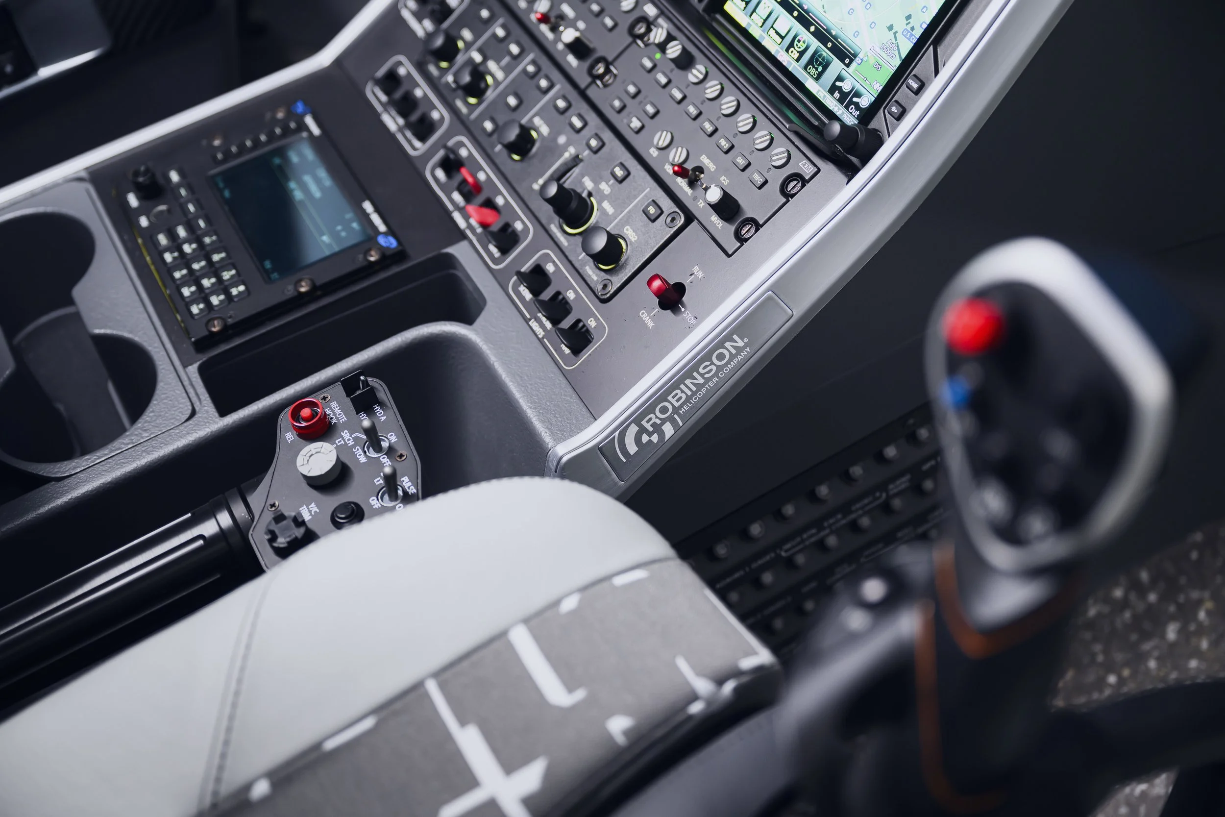 Close-up of control panel inside a Robinson helicopter cockpit, showing buttons, switches, and a screen.