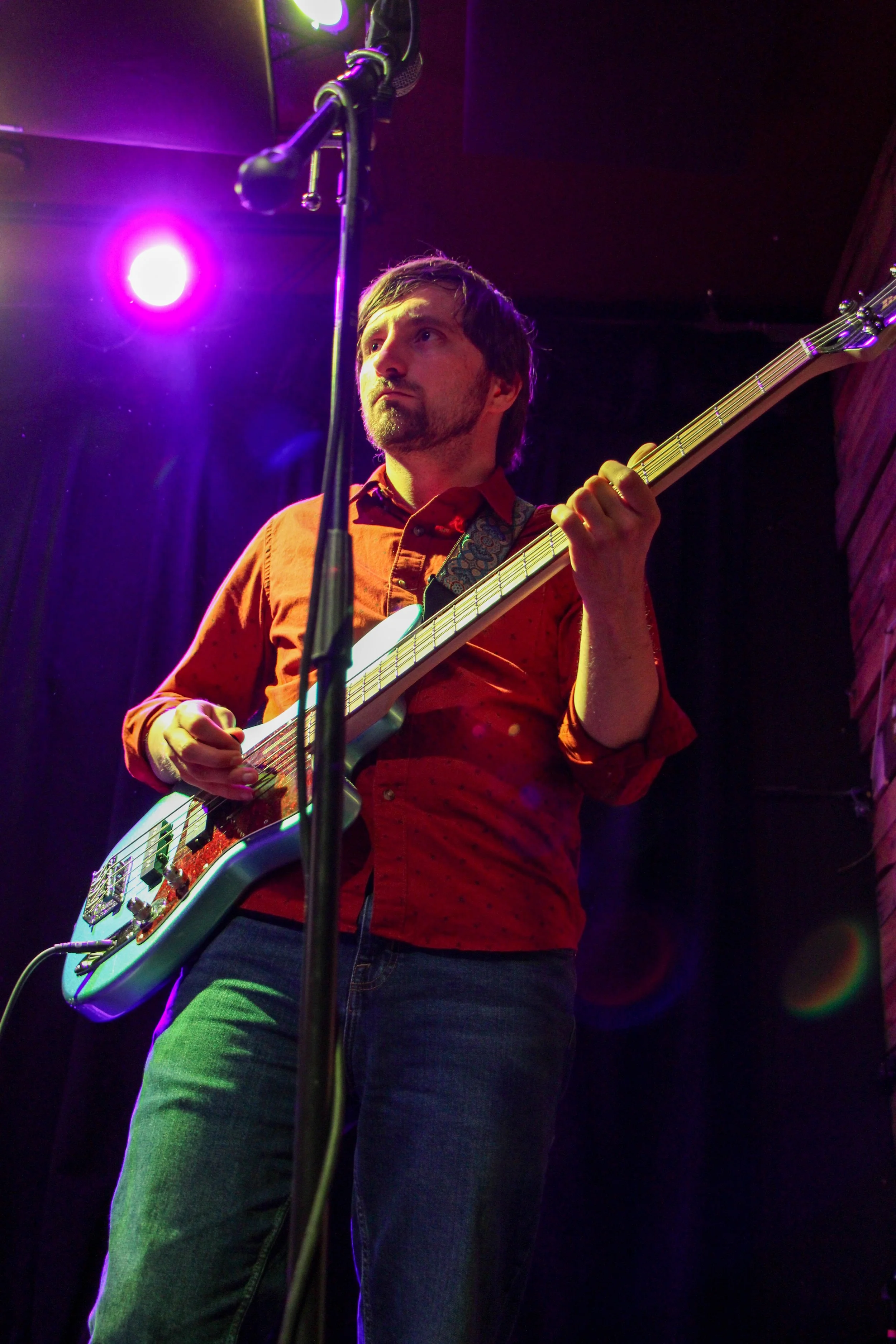A man playing an electric guitar on stage with purple and green lighting effects.