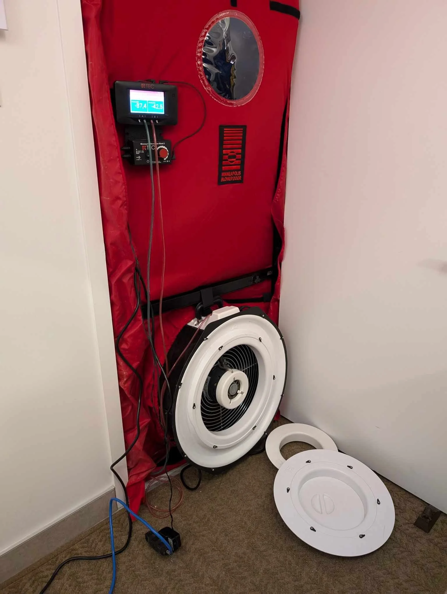 Un défibrillateur automatisé externe (DAE) rouge avec un écran numérique et un ventilateur ou un appareil de refroidissement à l'arrière. Une pièce de plafond blanc est visible sur le côté et un sol en moquette.