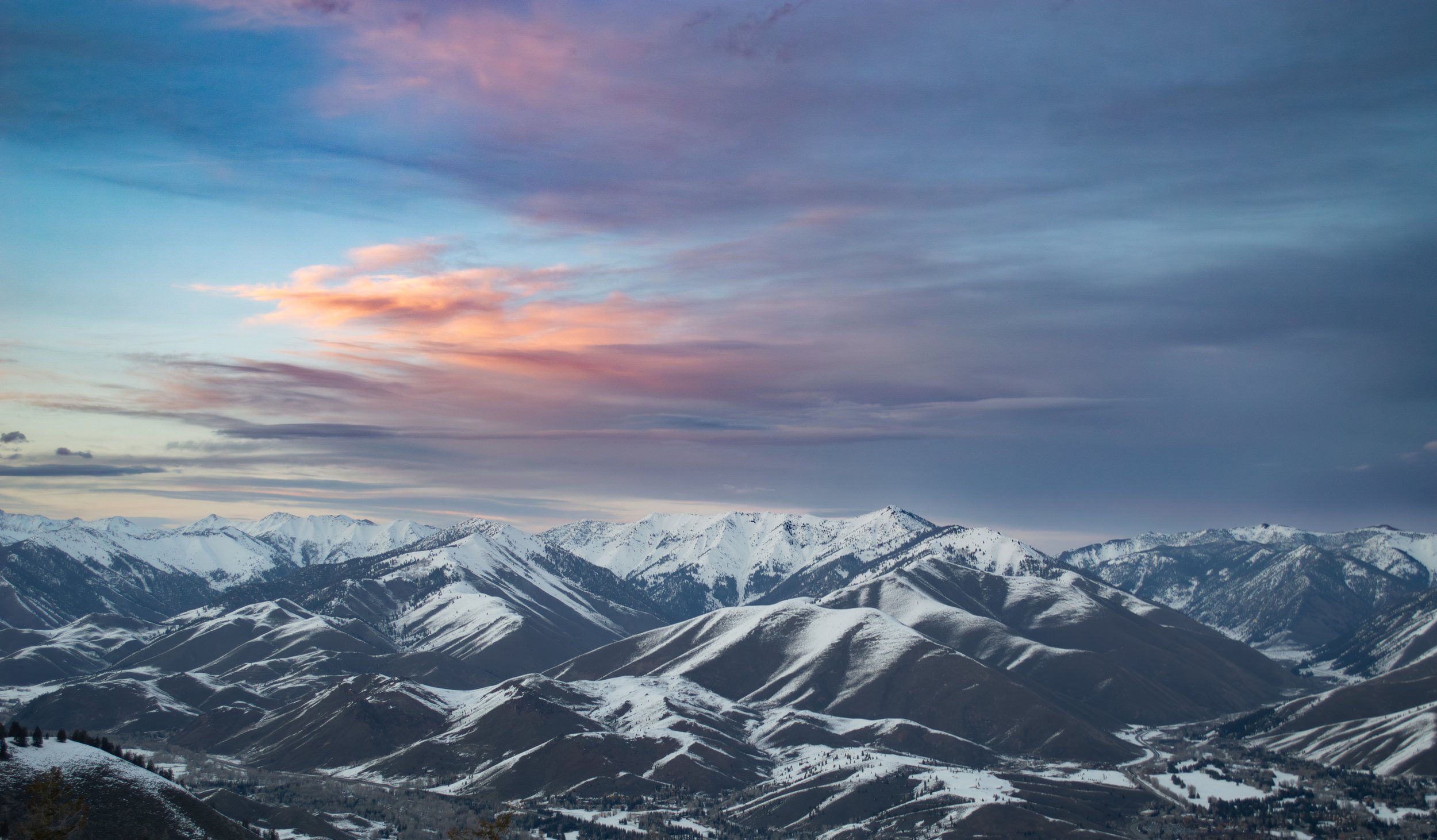 Snow-covered mountain range at sunset with colorful sky.