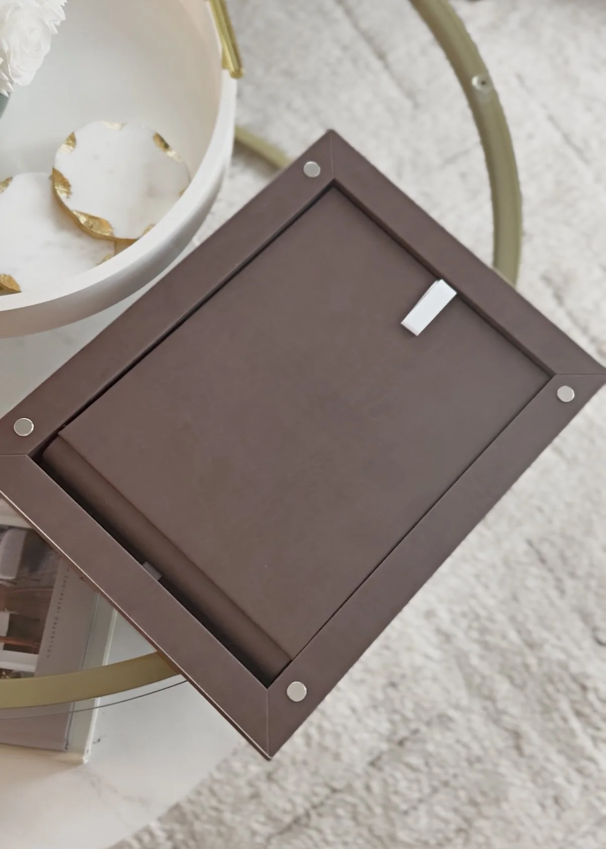 A brown rectangular box with a closed lid sitting on a white table next to a white bowl with gold-edged decorative plates inside.