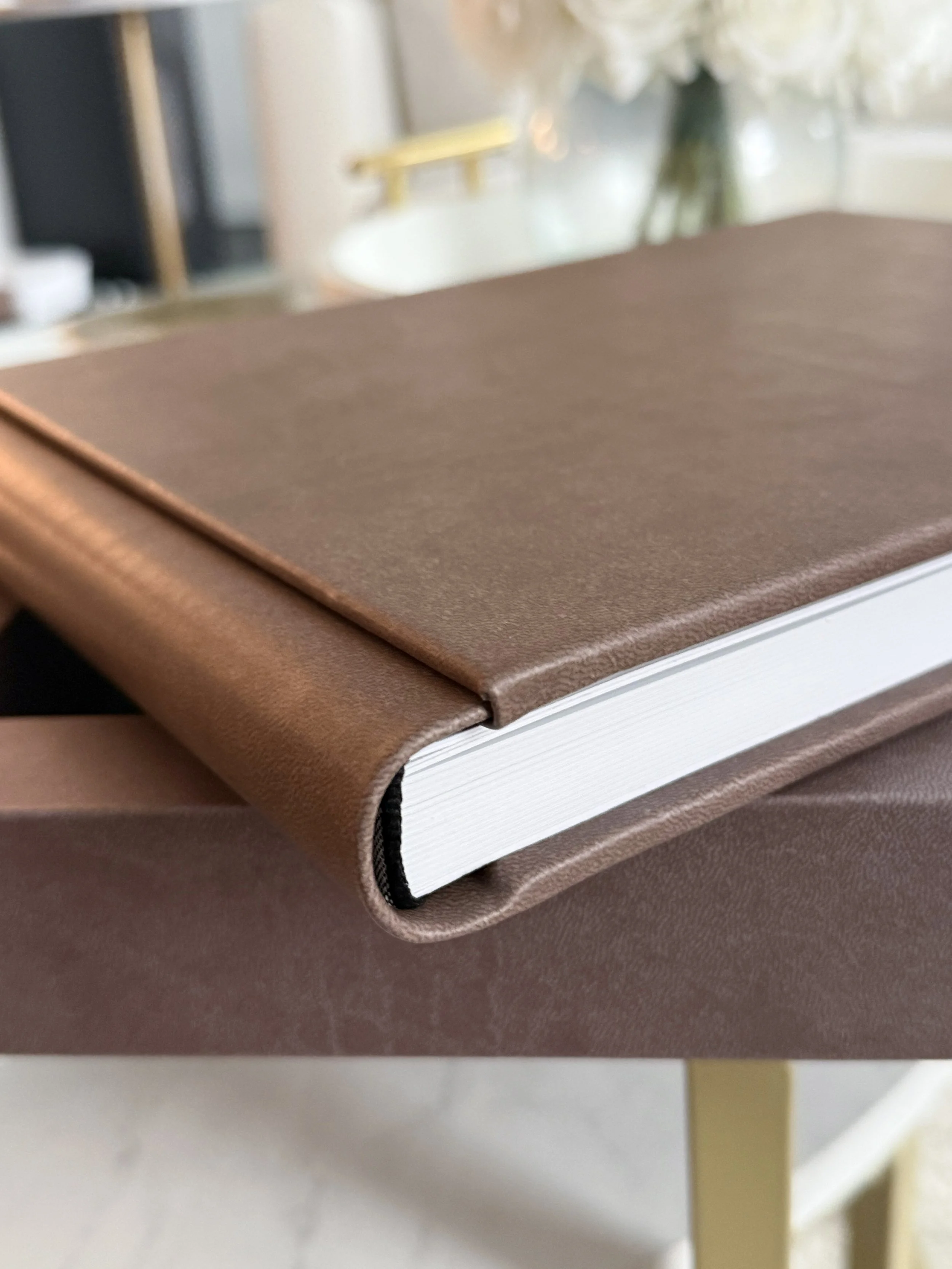 Close-up of a brown journal or diary with a leather-like cover, resting on a matching surface, with white pages visible at the binding.