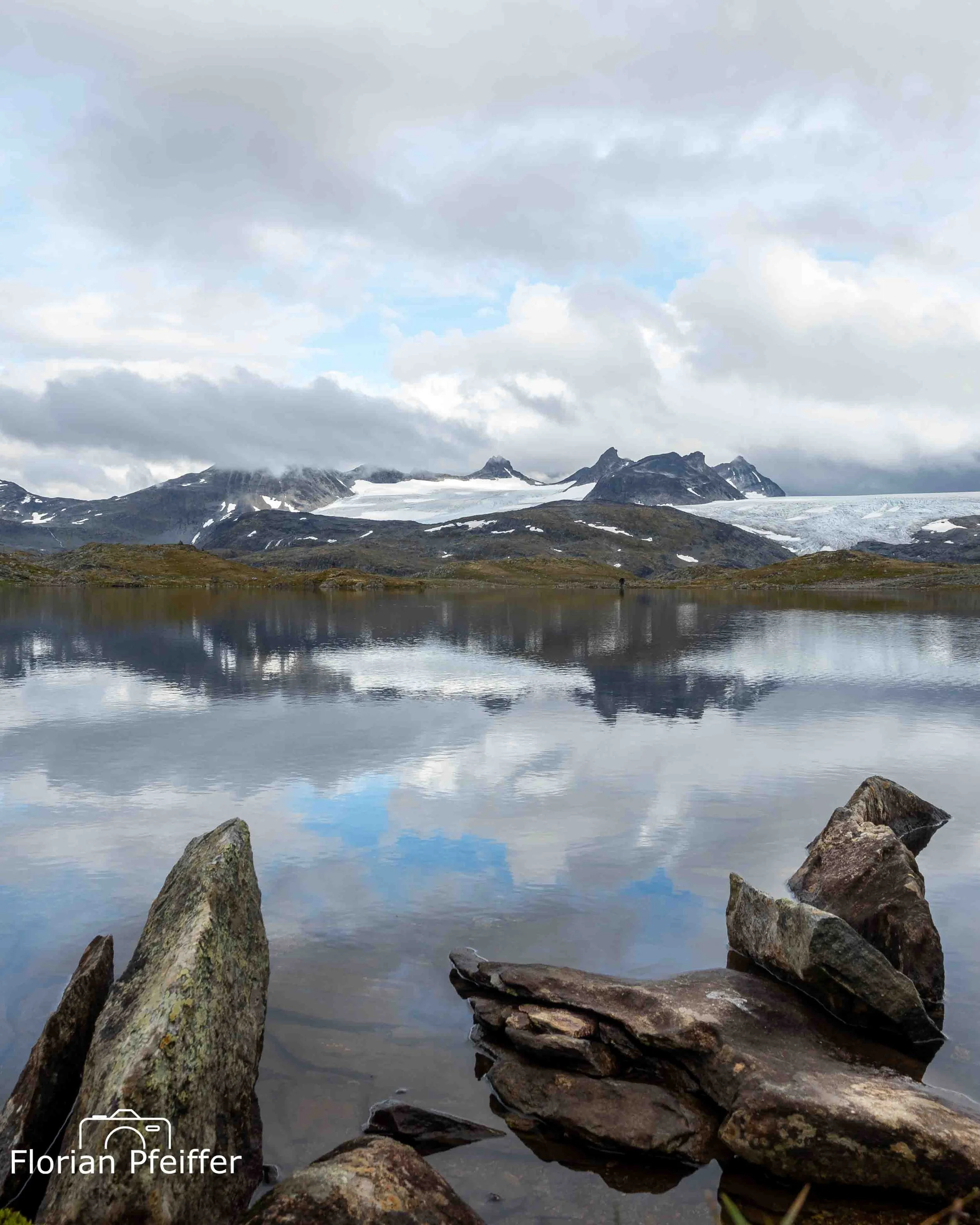 landscape image of a mountain ridge and a lake with rocks in the foreground