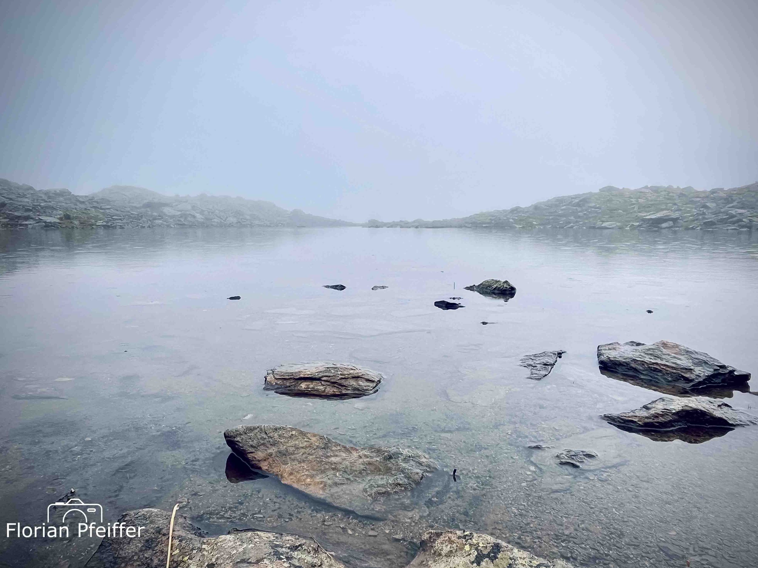 a lake with big rocks and fog