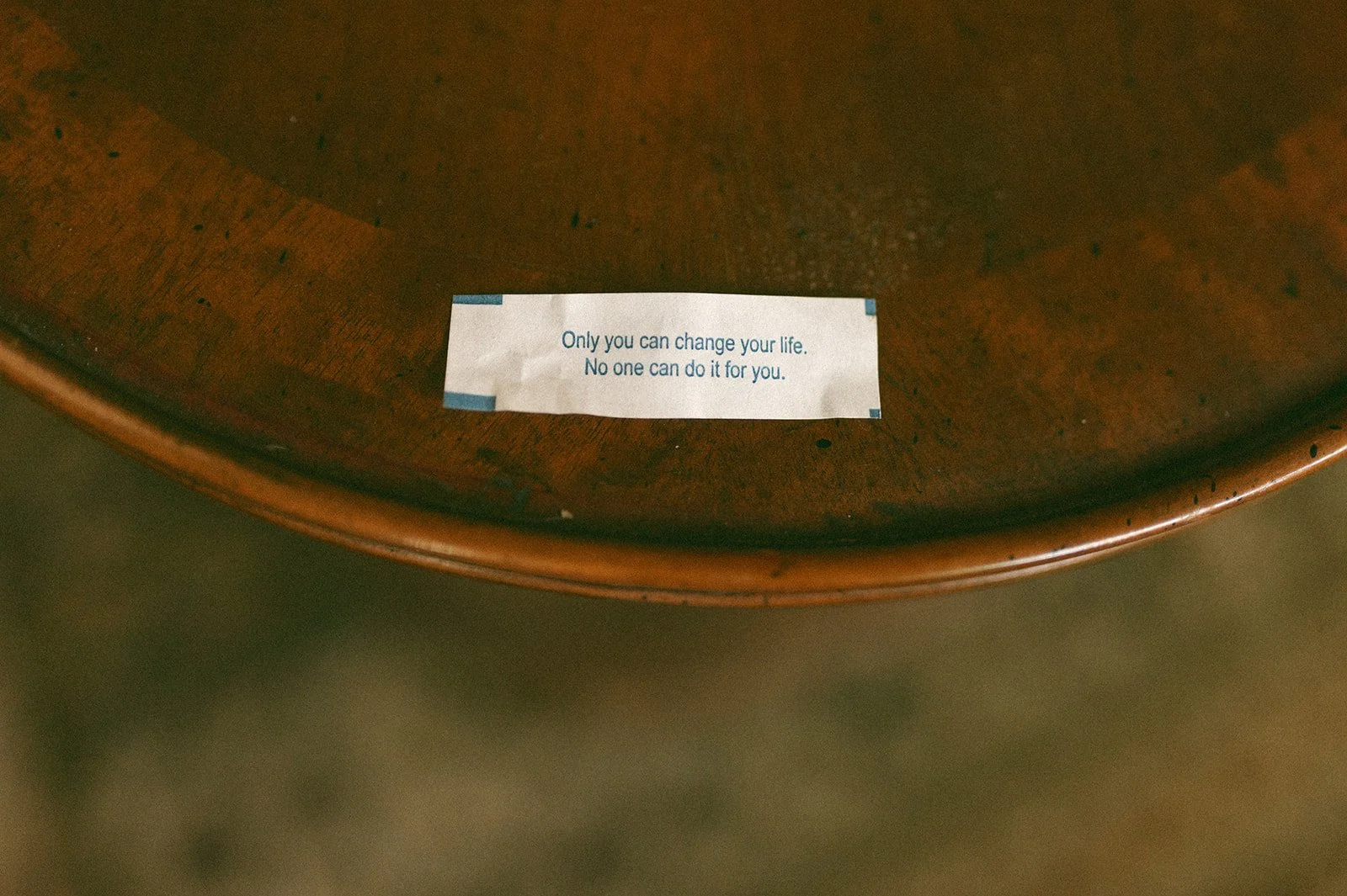 A small piece of paper with the quote 'Only you can change your life. No one can do it for you,' placed on a wooden surface.