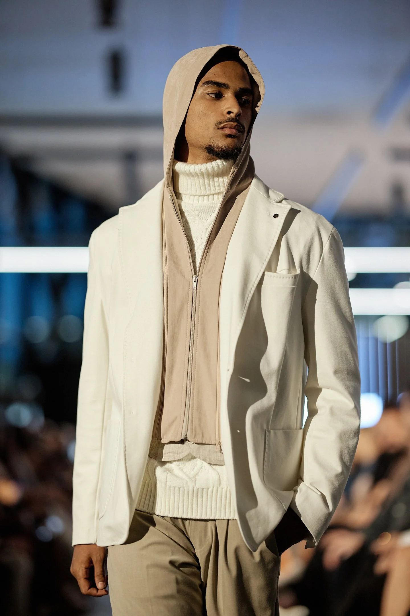 Silhouette masculine M3 Montréal 2025 :veste blanche structurée superposée à un col roulé texturé, pantalon beige fluide, avec une capuche légère taupe pour un look contemporain et minimaliste.