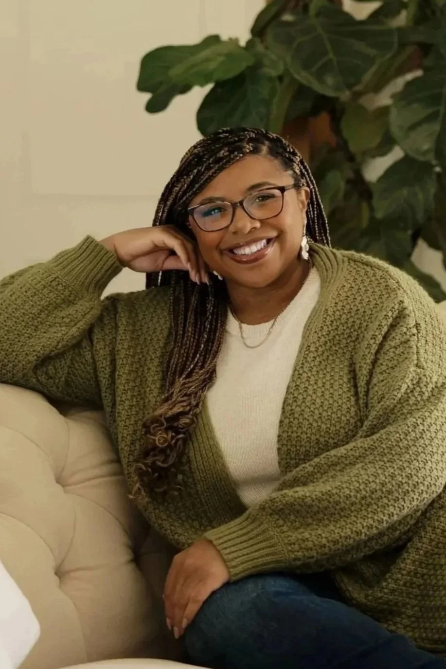 Black woman therapist sitting on a stool with hands crossed in front of her with warm welcoming smile