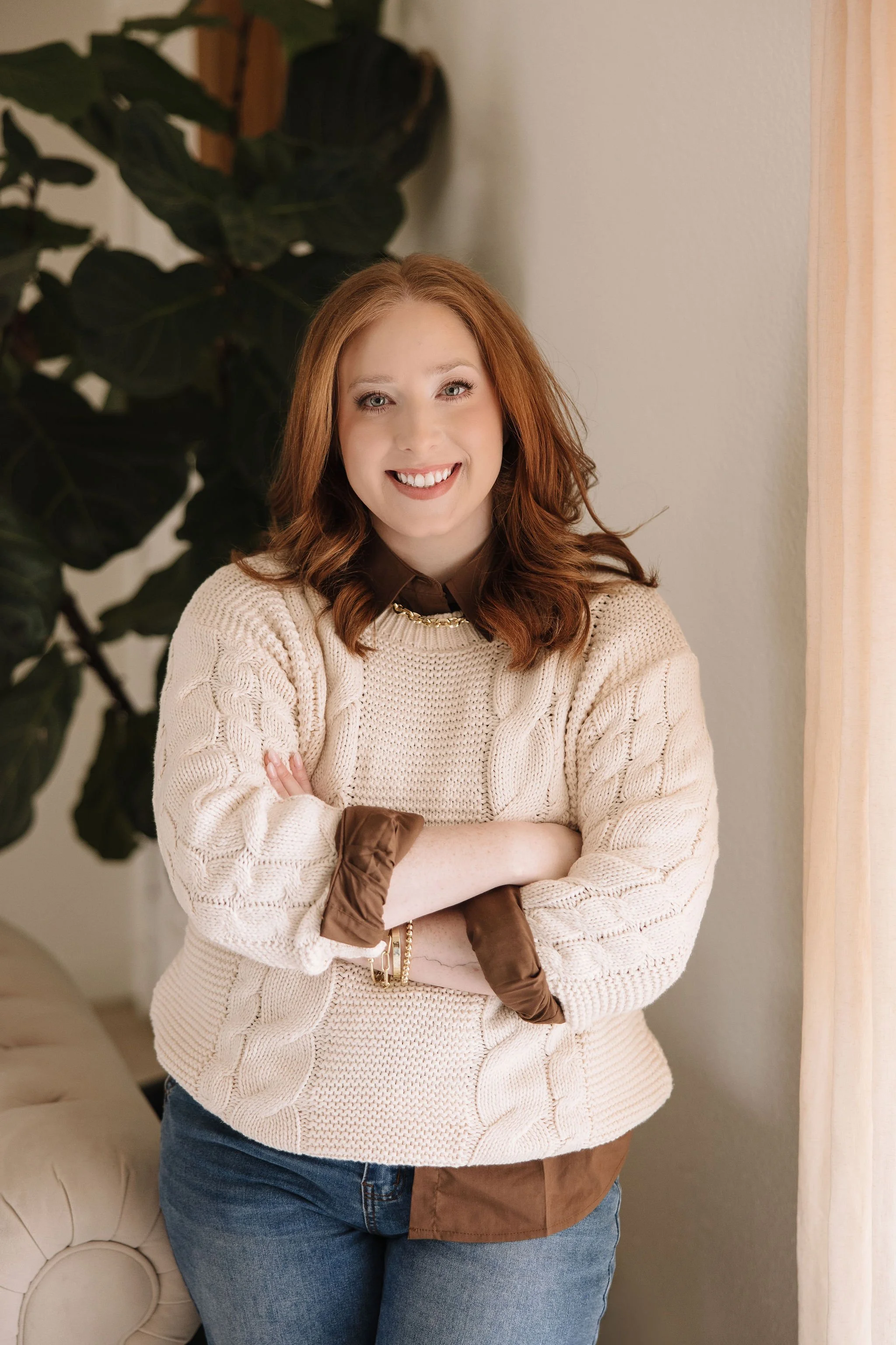 Woman, Red Headed Therapist sitting on therapy couch with hands crossed in front of her with warm welcoming smile