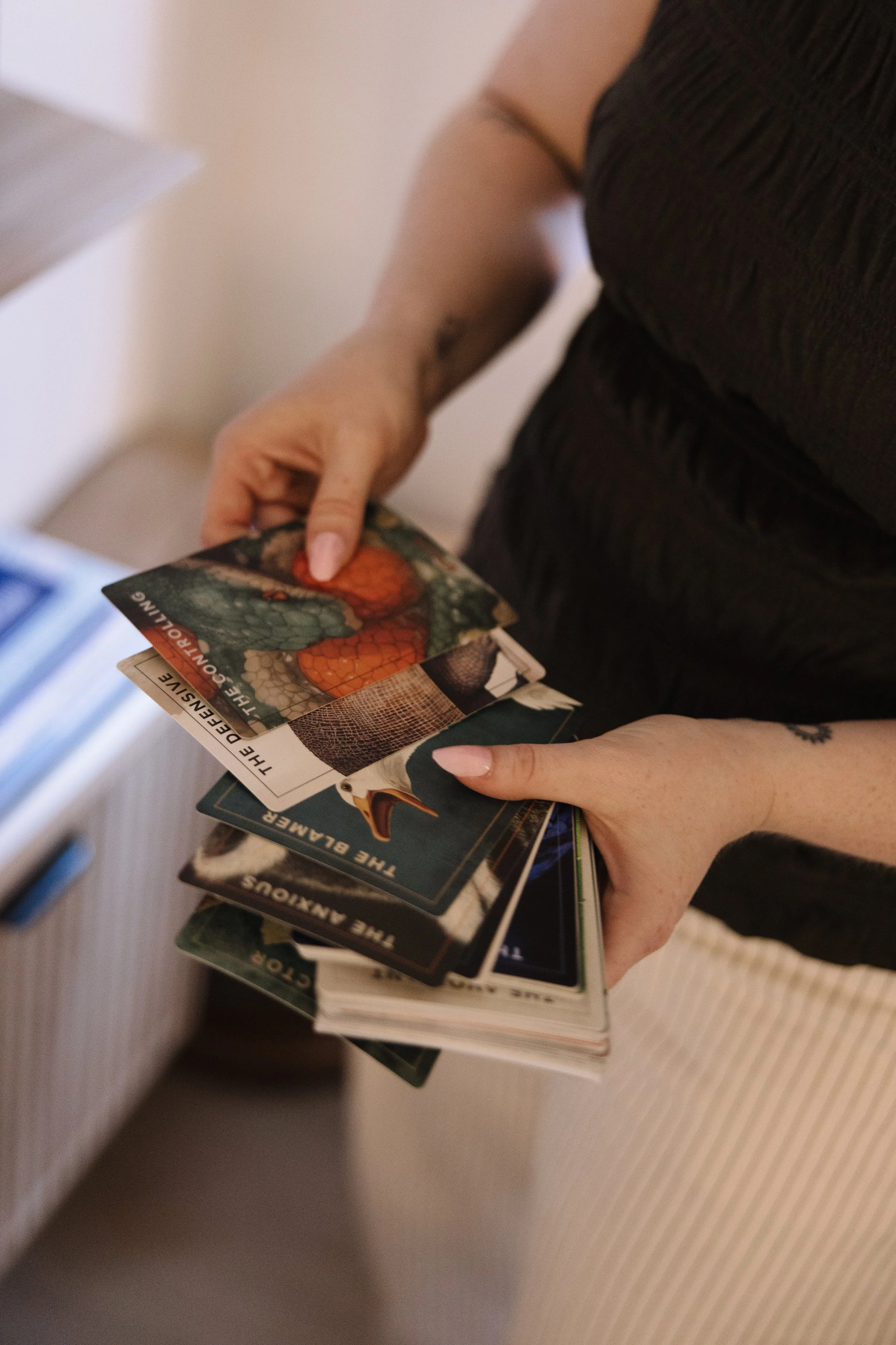 Person holding a stack of books and trading cards, with a focus on a card featuring a colorful image of a dragon.